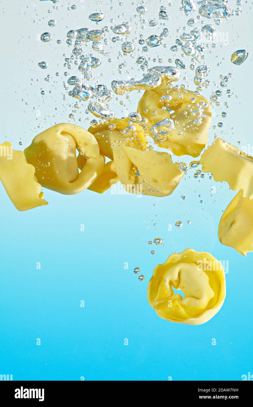 Tortellini fallen in das Wasser, mit Luftblasen, auf einem blauen Hintergrund. Stockfoto
