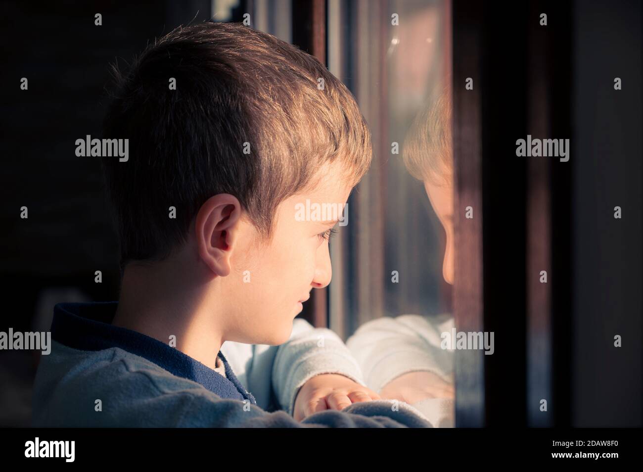 Kleiner Junge mit Blick aus dem Fenster auf den Sonnenaufgang am Herbsttag. Krankheit Kind in Quarantäne zu Hause. Stockfoto