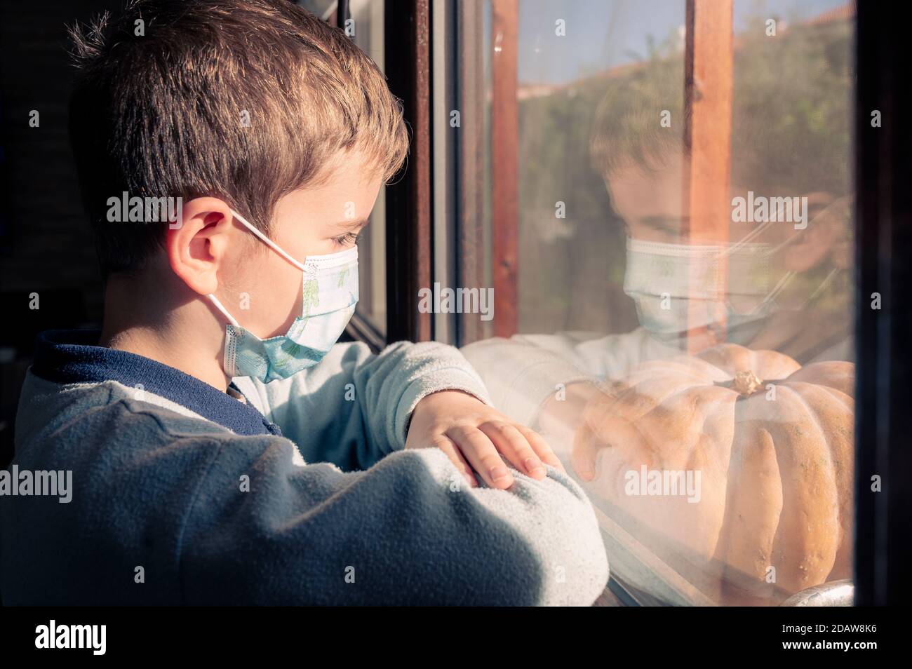 Krankheit Kind in Quarantäne zu Hause. Junge tragen schützende medizinische Masken sitzt auf Fensterbank und schaut aus dem Fenster. Virenschutz, Coronavirus-Pandemie, p Stockfoto