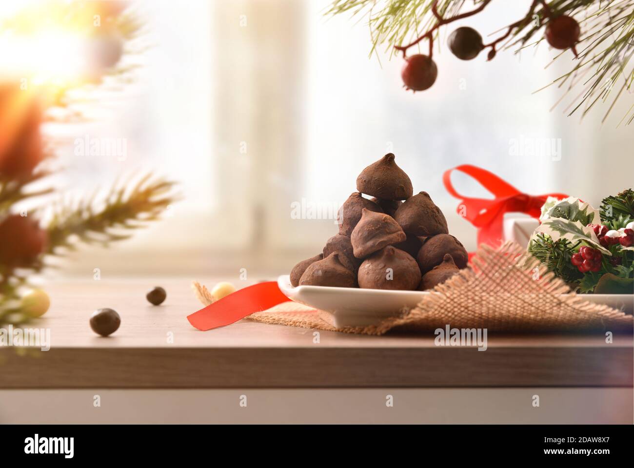 Weihnachtliches dekoratives Herzstück auf Holzsockel mit Teller voller Schokoladentrüffel neben einem Fenster. Vorderansicht. Horizontale Zusammensetzung. Stockfoto