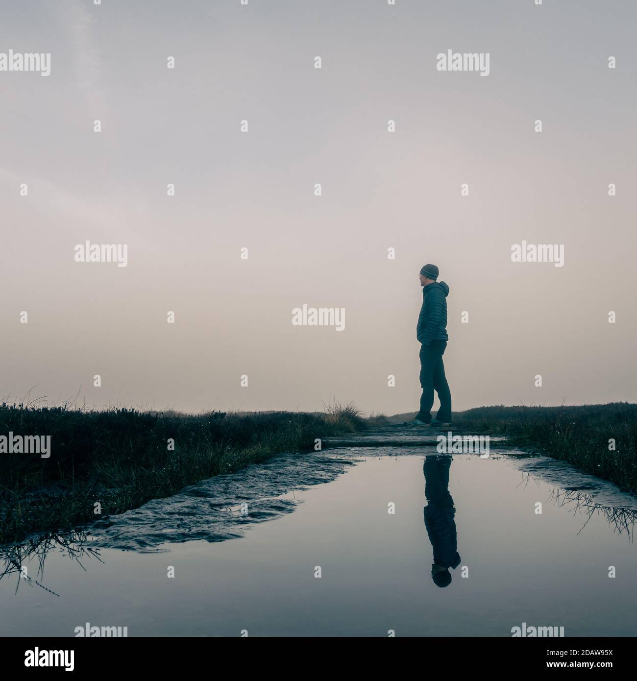 Low-Angle-Ansicht einer Person, die in der Landschaft im Freien, Blick in den Nebel mit ihrer Reflexion in einer Pfütze auf dem Weg, England Stockfoto