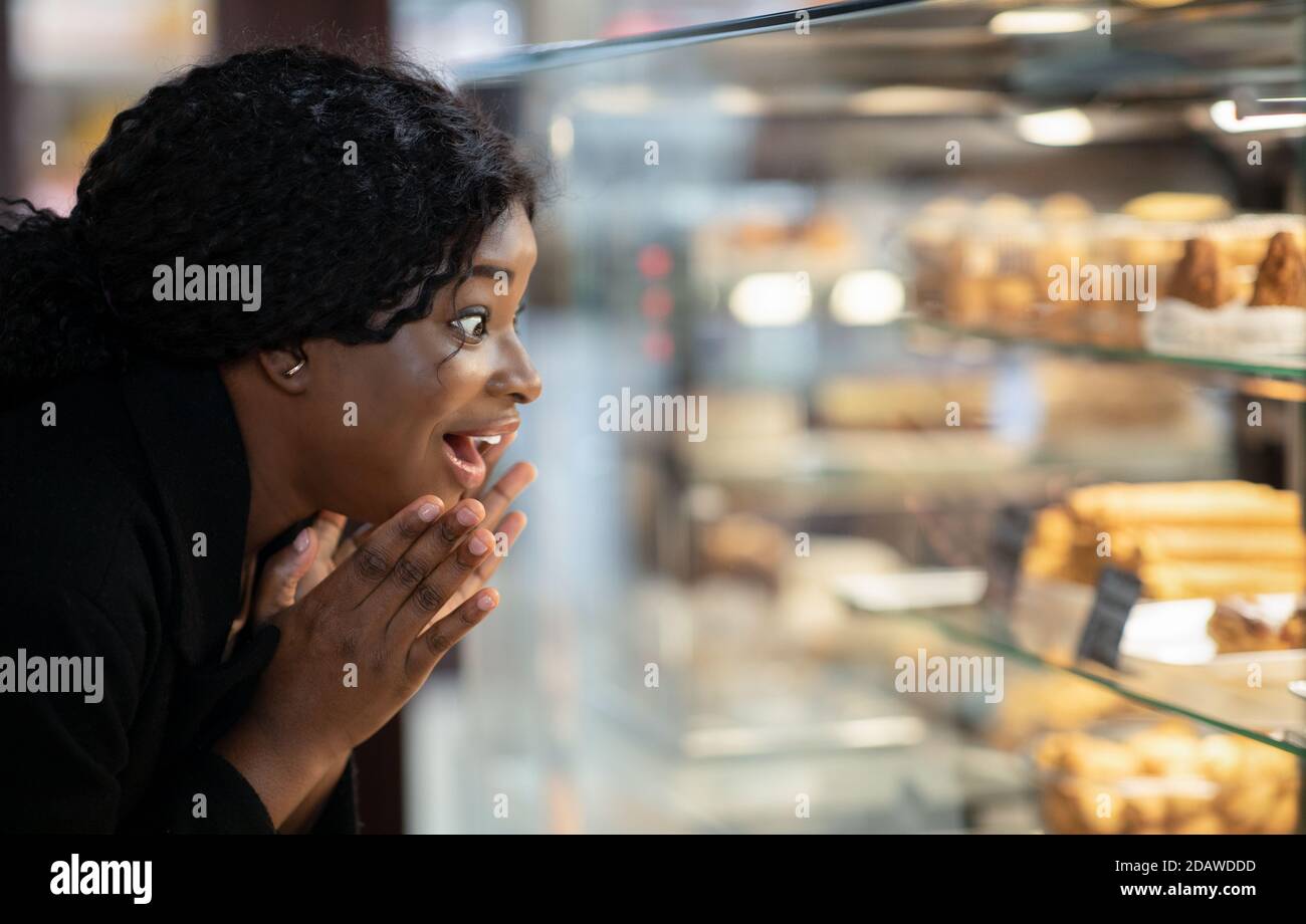 Überrascht erstaunt glücklich afroamerikanischen Millennial Dame mit offenem Mund Blick auf Schaufenster mit Desserts Stockfoto