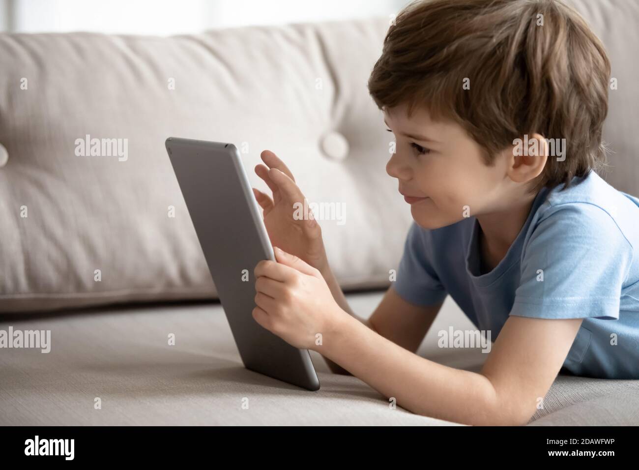 Nahaufnahme kleiner Junge mit Computer-Tablet, auf der Couch liegen Stockfoto