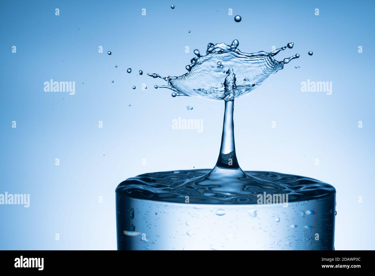 Wassertropfen, der aus einem isolierten hellblauen Hintergrund in Glas spritzt Stockfoto