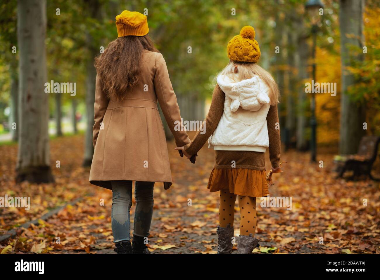 Hallo Herbst. Von hinten gesehen moderne Mutter und Tochter in orangen Hüten im Freien auf dem Stadtpark im Herbst genießen Promenade. Stockfoto