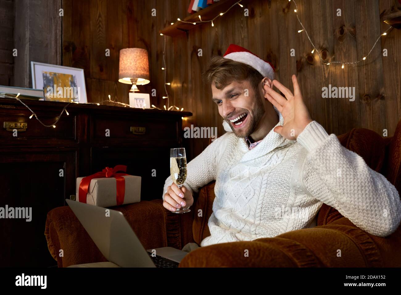 Glücklich junger Mann winkt Hand feiert virtuelle Neujahrsparty mit Laptop. Stockfoto