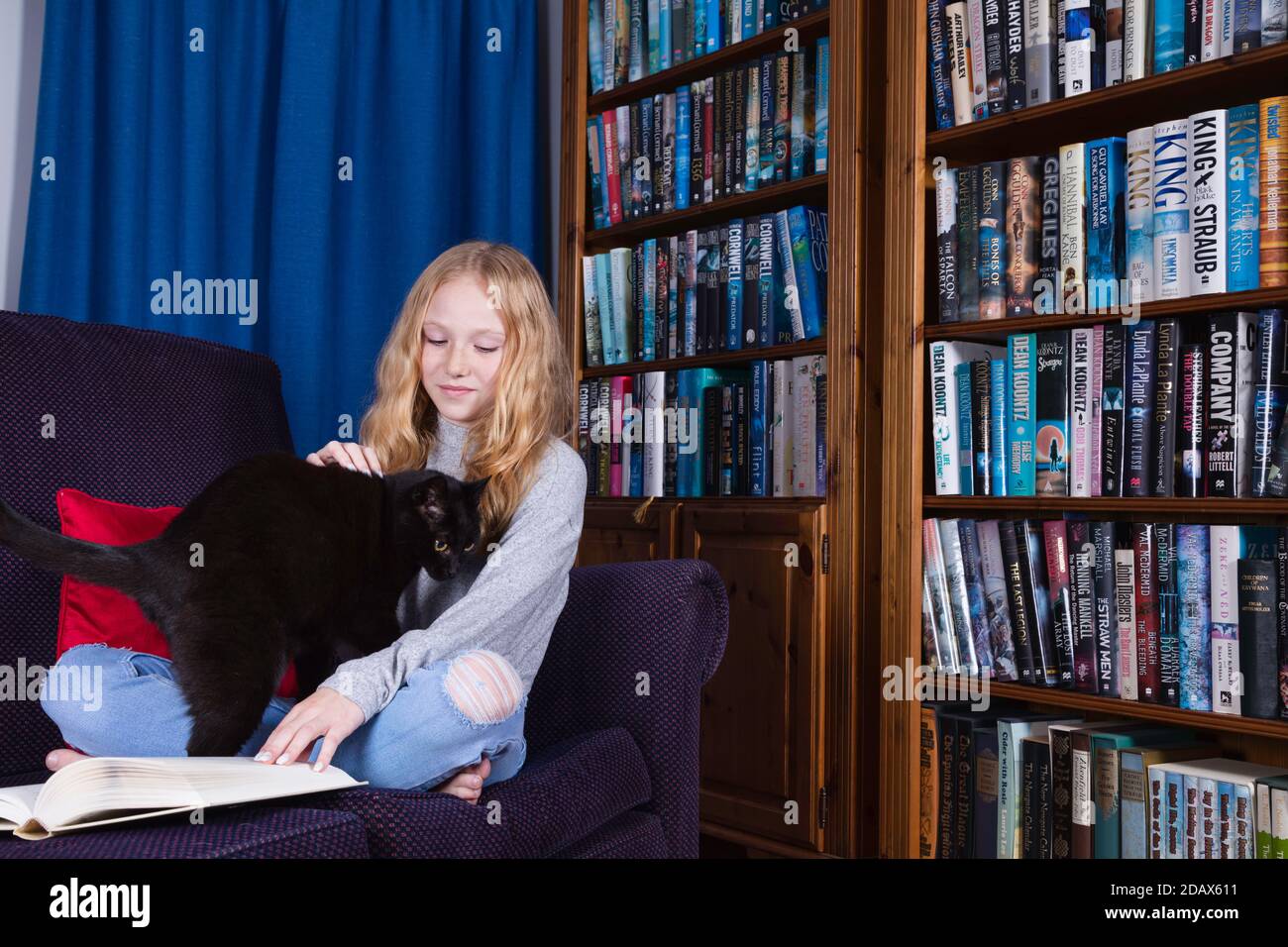 Pre-teen, fair haired junges Mädchen versucht zu lesen, aber ihre Katze wird sie nicht zulassen. Stockfoto