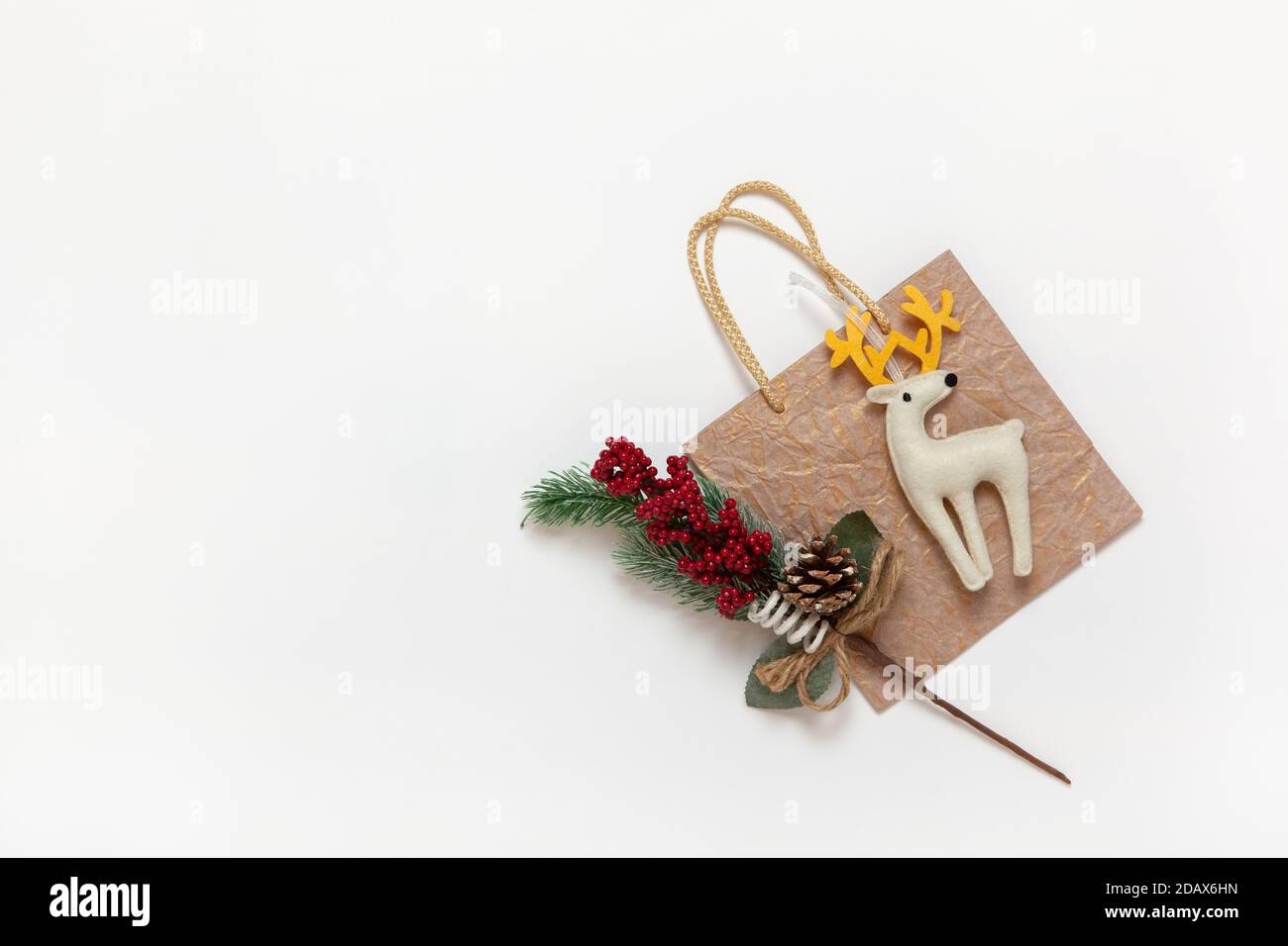 Goldene Weihnachts-Geschenktasche, weißer Filzspielzeug-Hirsch mit gelben Hörnern, Zweig mit roten Beeren und Nadeln auf weißem Hintergrund, Kopierraum. Festlich, Neujahr Stockfoto