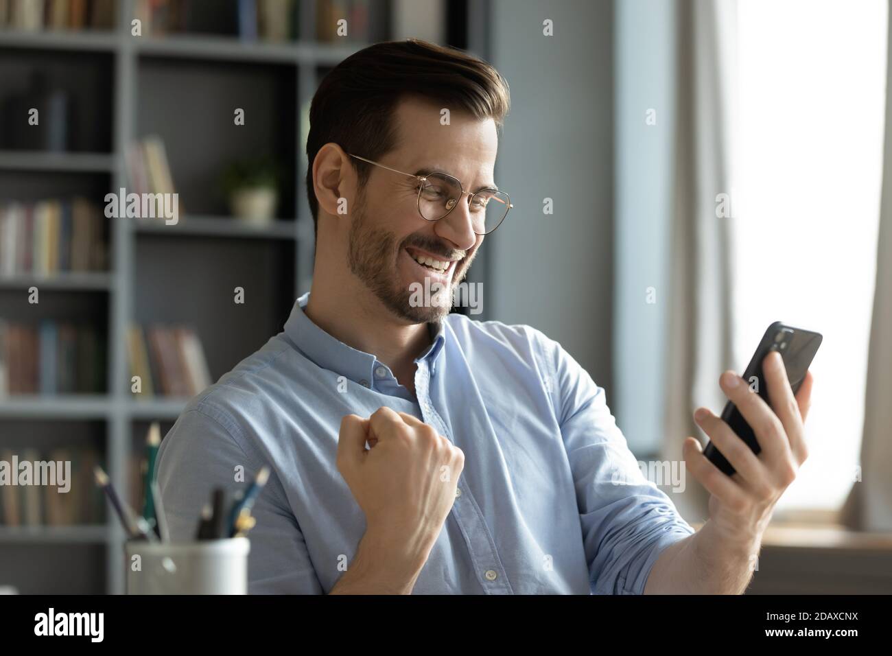 Glücklicher Mann hält Smartphone Nachricht lesen Feiern Sie gute Nachrichten online Stockfoto