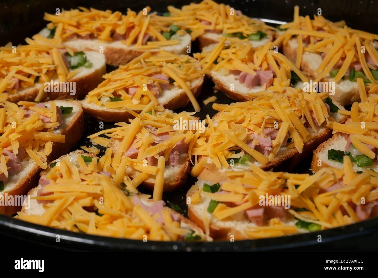 Viele hausgemachte Sandwiches mit Würstchen und lang geschnittenem Käse auf der großen schwarzen Metallterrasse vor dem thermischen Kochen, Home Fast-Food-Konzept, Nahaufnahme Stockfoto