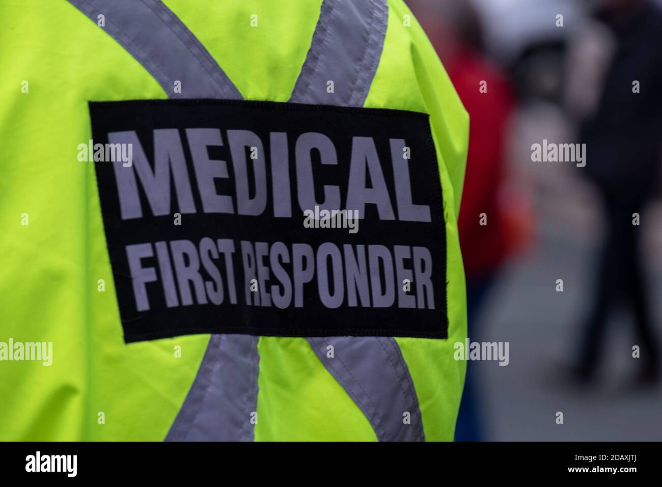 Medizinischer Ersthelfer trägt eine leuchtend gelbe Uniform mit den Worten medizinischer Ersthelfer auf dem Rücken in grauen Buchstaben mit schwarzem Hintergrund. Stockfoto