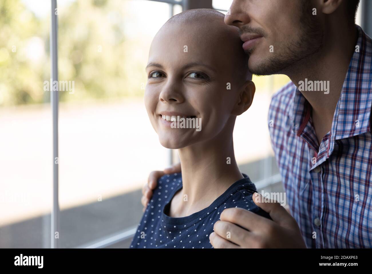 Optimistische junge Frau, die eine Krebsbehandlung erhält, umarmt vom geliebten Mann Stockfoto