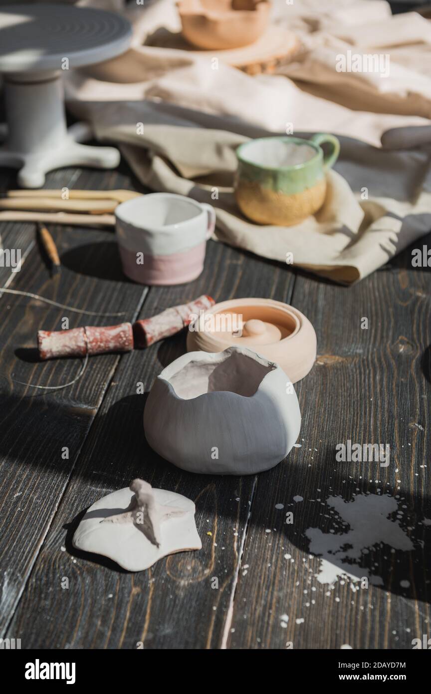 Eine Nahaufnahme von Tontafeln und einem Pinsel auf einem Holztisch und getrockneten Blumen auf einem Hintergrund. Gearbeitetes Geschirr in einem Töpferstudio. Handgefertigt Stockfoto