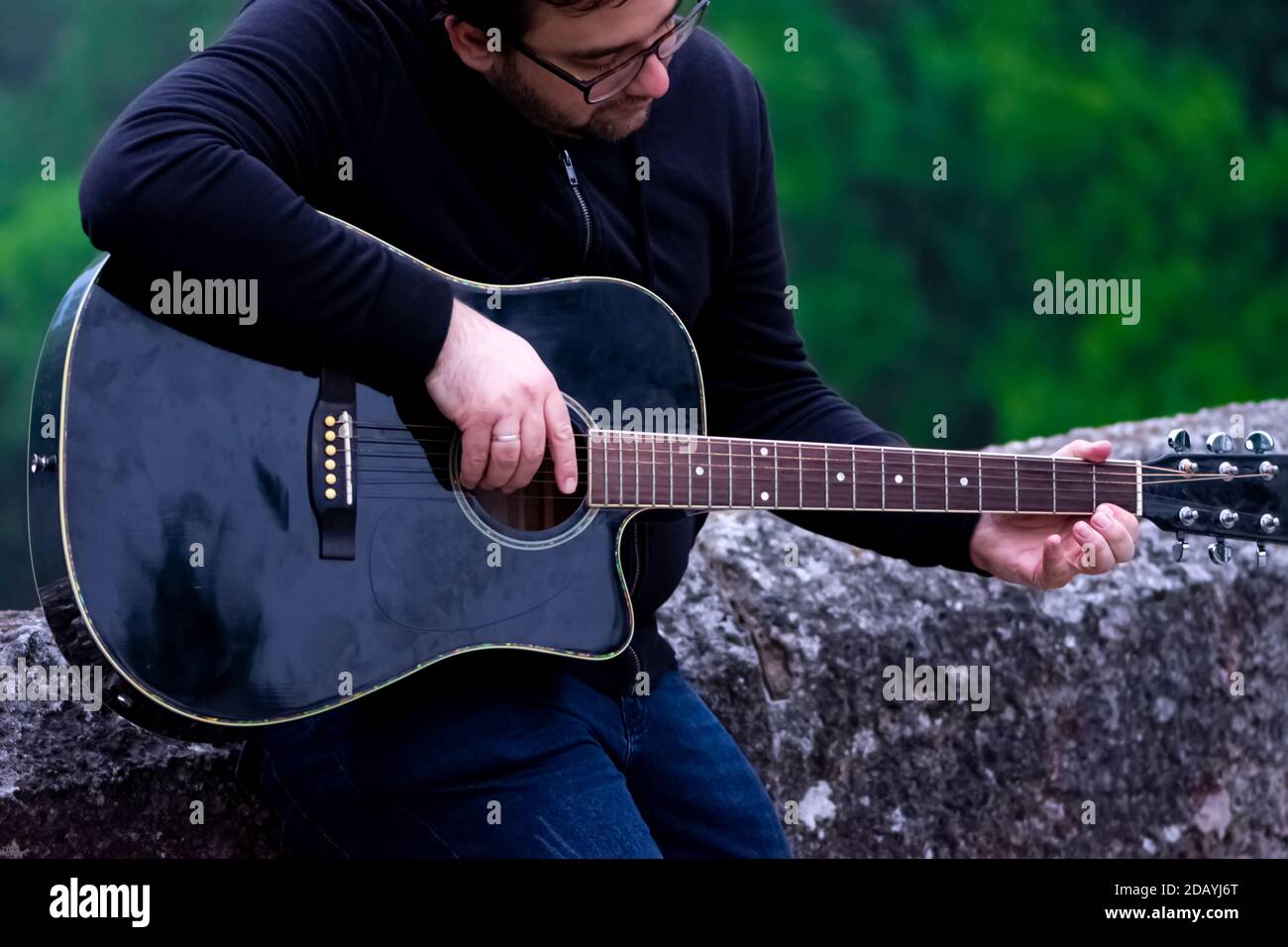 Junger Mann spielt akustierende Gitarre und lehnt sich an die Brücke Stockfoto