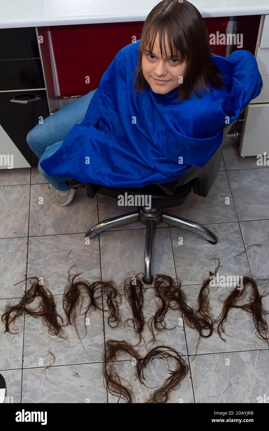 Portrait von niedlichen jungen Mädchen mit neuer Frisur und Namen Auf dem Boden von geschnittenen Haaren geschrieben Stockfoto