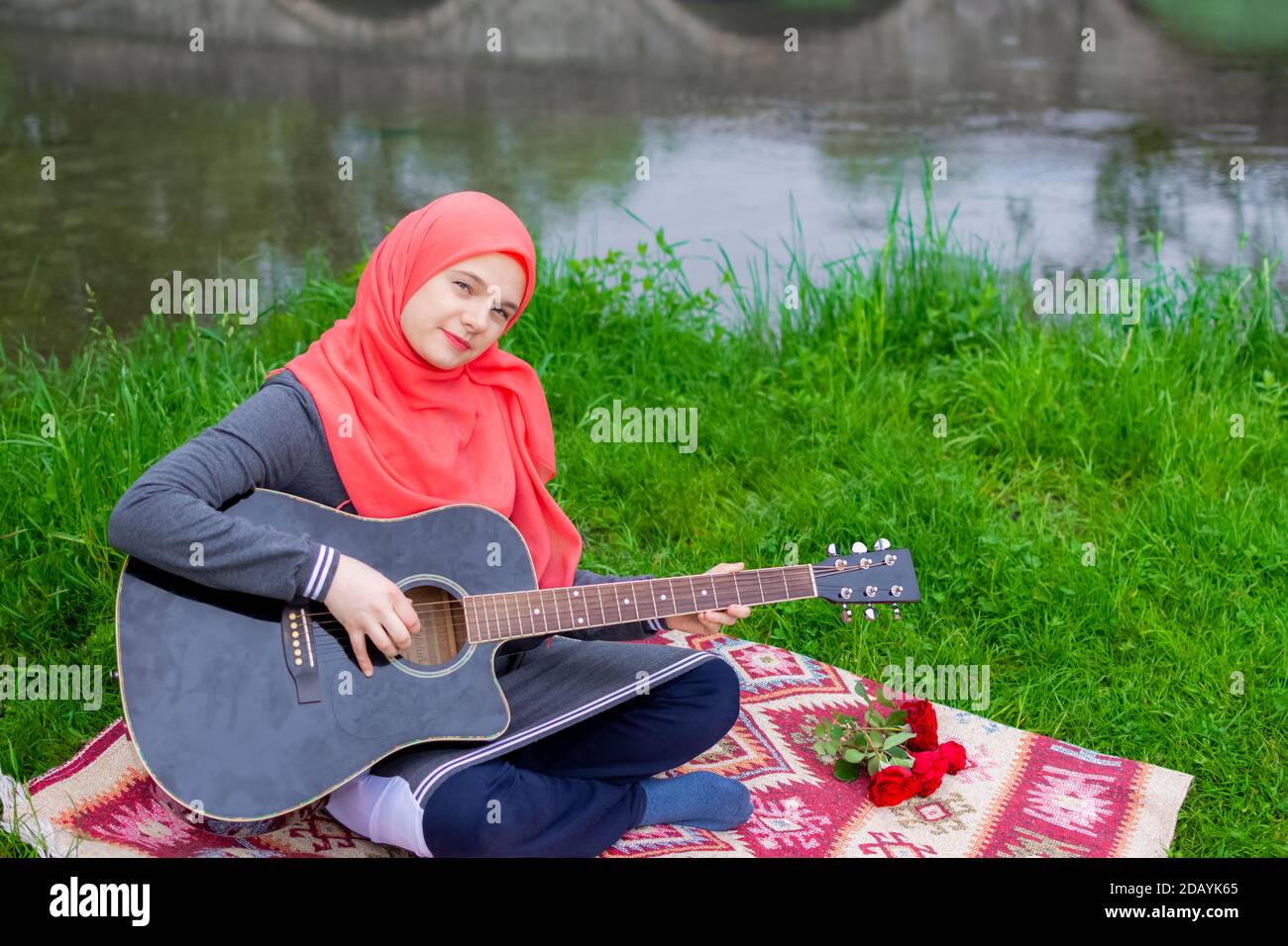 Preaty junge muslimische Mädchen traying akustische Gitarre am Flussufer zu spielen Stockfoto