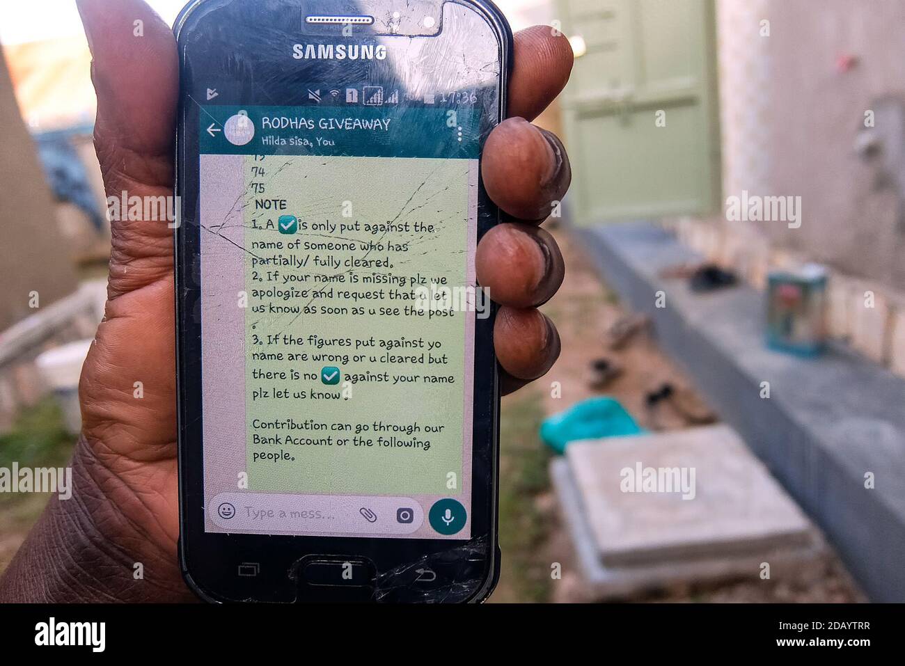 Steven Niwareeba liest eine Nachricht von einer der WhatsApp-Gruppen, zu denen er in Uganda gehört. Stockfoto