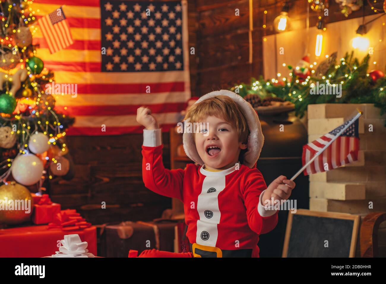 American Santa Junge feiern weihnachten zu Hause. Freude und Glück. Schönen Urlaub. Geschenk-Box. Kleiner Junge in Weihnachtsmütze und Kostüm mit Spaß Stockfoto