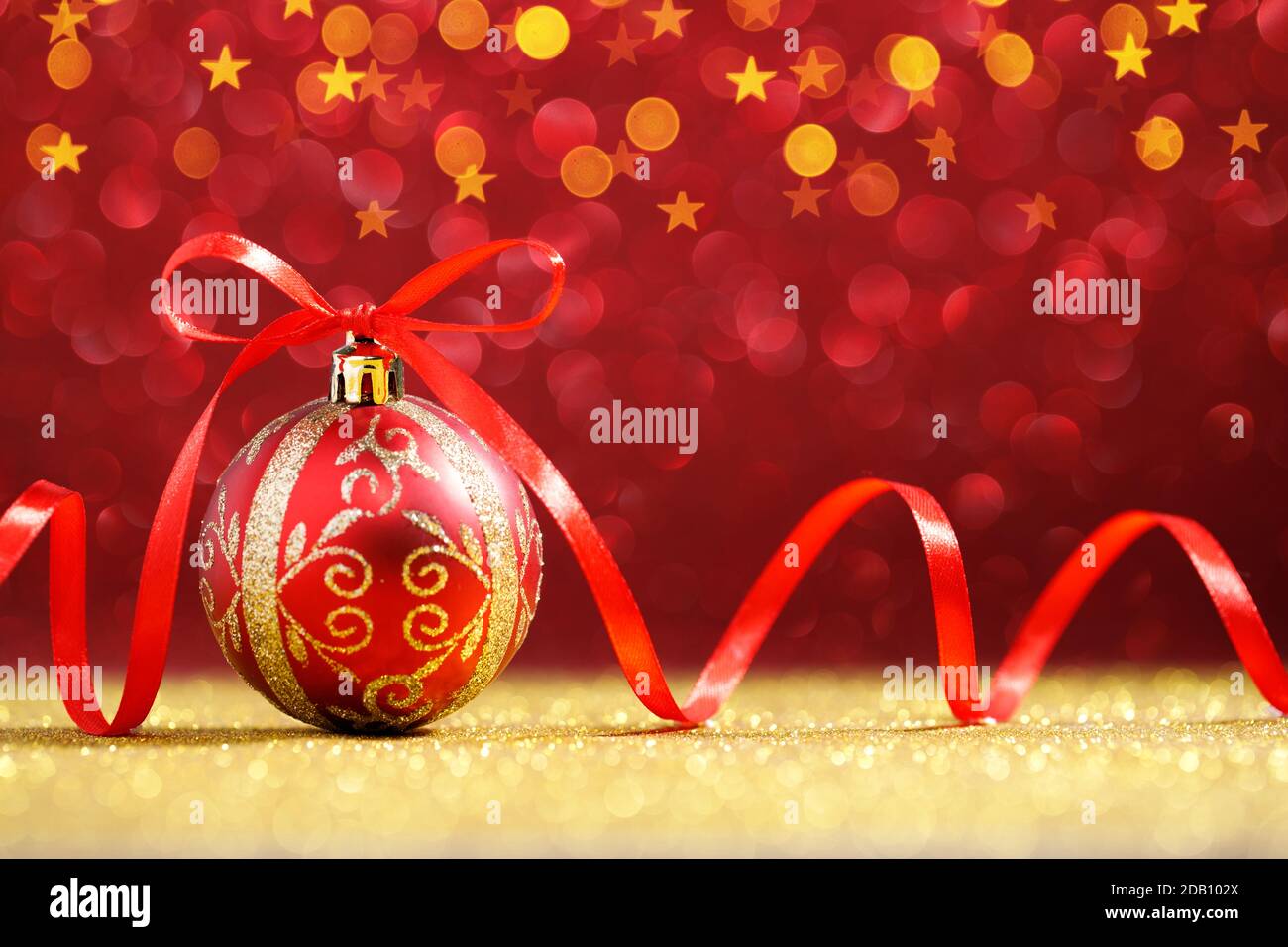 Rote weihnachtskugel mit roter Schleife auf goldenem Glitzer Stockfoto