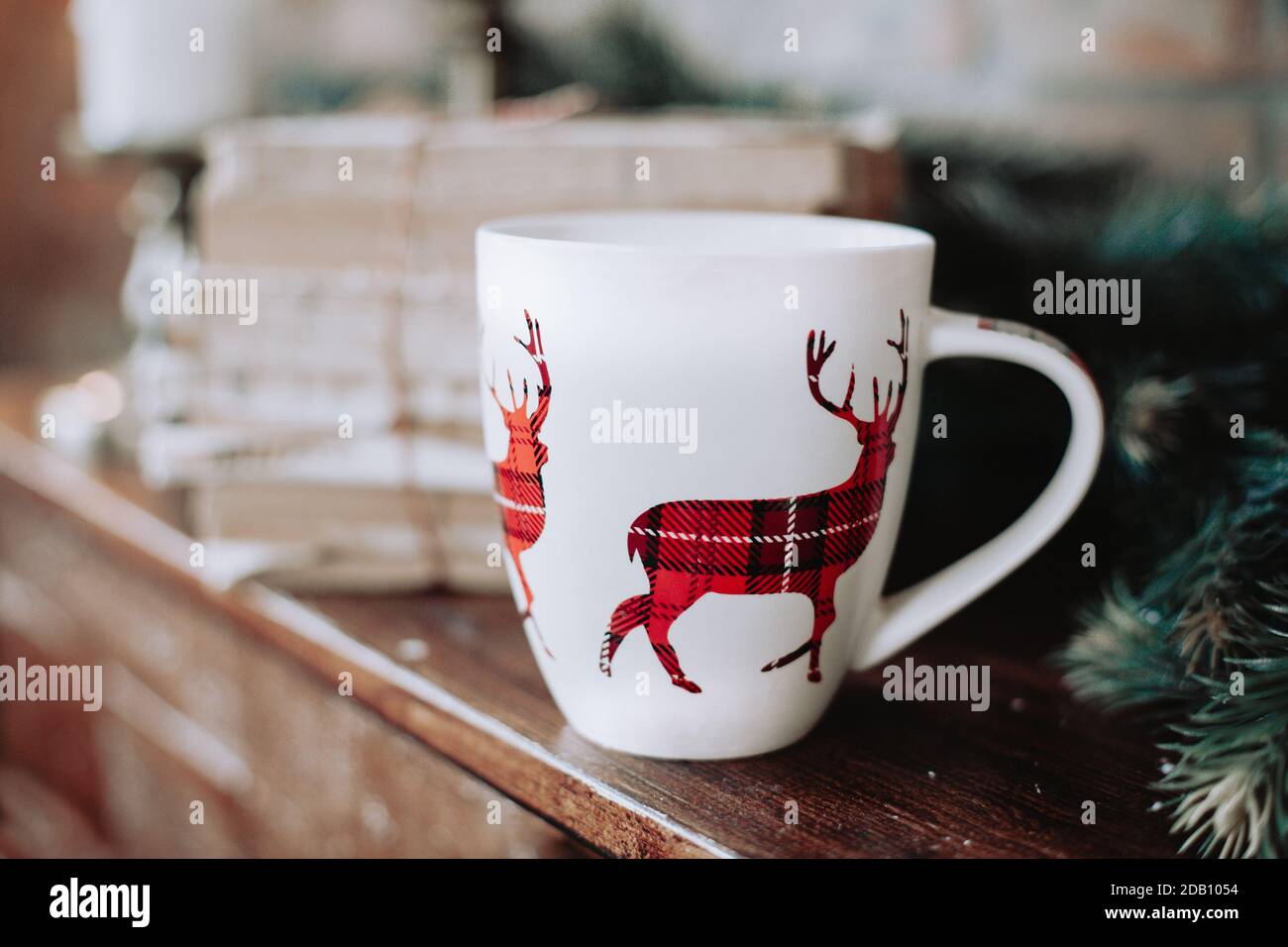 Weihnachtsbecher mit einem rot karierten Rentier auf einem Kamin mit Vintage-Büchern. Rustikal, gemütlich, Winterweihnachtsstimmung. Stockfoto