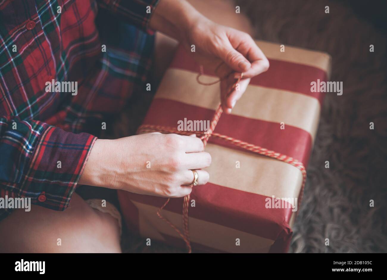 Frau Verpackung Weihnachtsgeschenke sitzen auf dem Boden in einem roten karierten Hemd. Rustikale Weihnachtsstimmung. Stockfoto