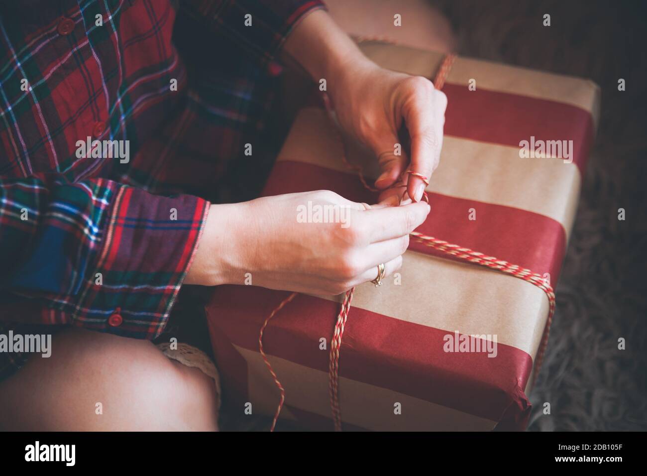 Frau Verpackung Weihnachtsgeschenke sitzen auf dem Boden in einem roten karierten Hemd. Rustikale Weihnachtsstimmung. Stockfoto