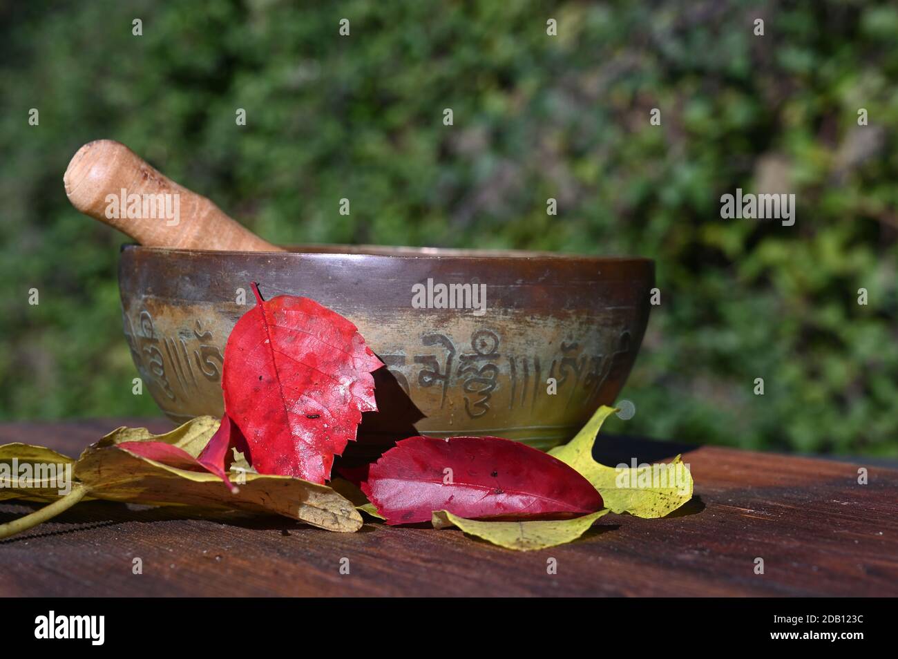 Eine singende Schüssel mit Herbstblättern auf einem Holzbrett Stockfoto