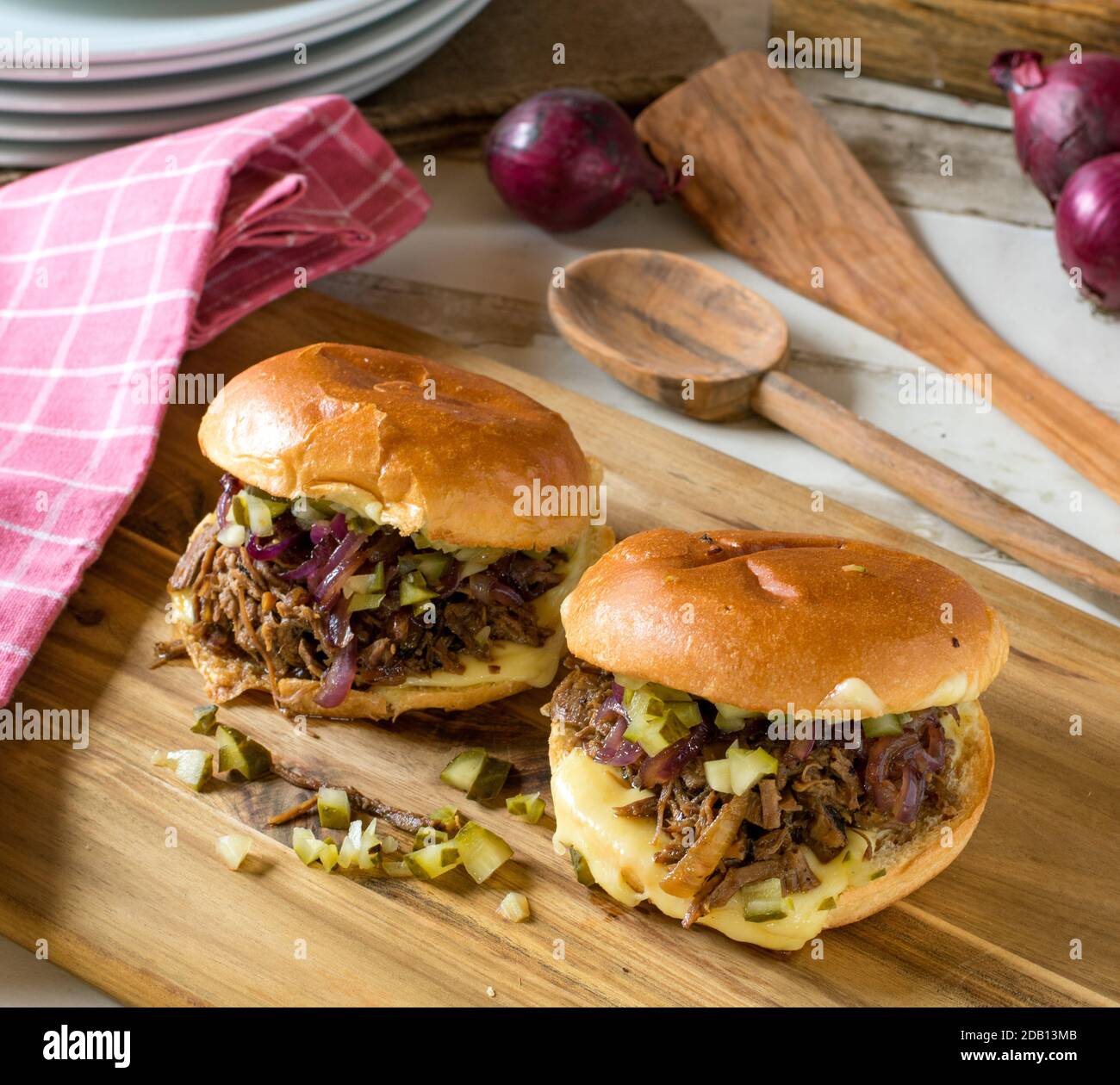 Hausgemachter Pulled Beef Burger mit karamellisierten roten Zwiebeln, Gurken und Käse auf einem Holzbrett Stockfoto