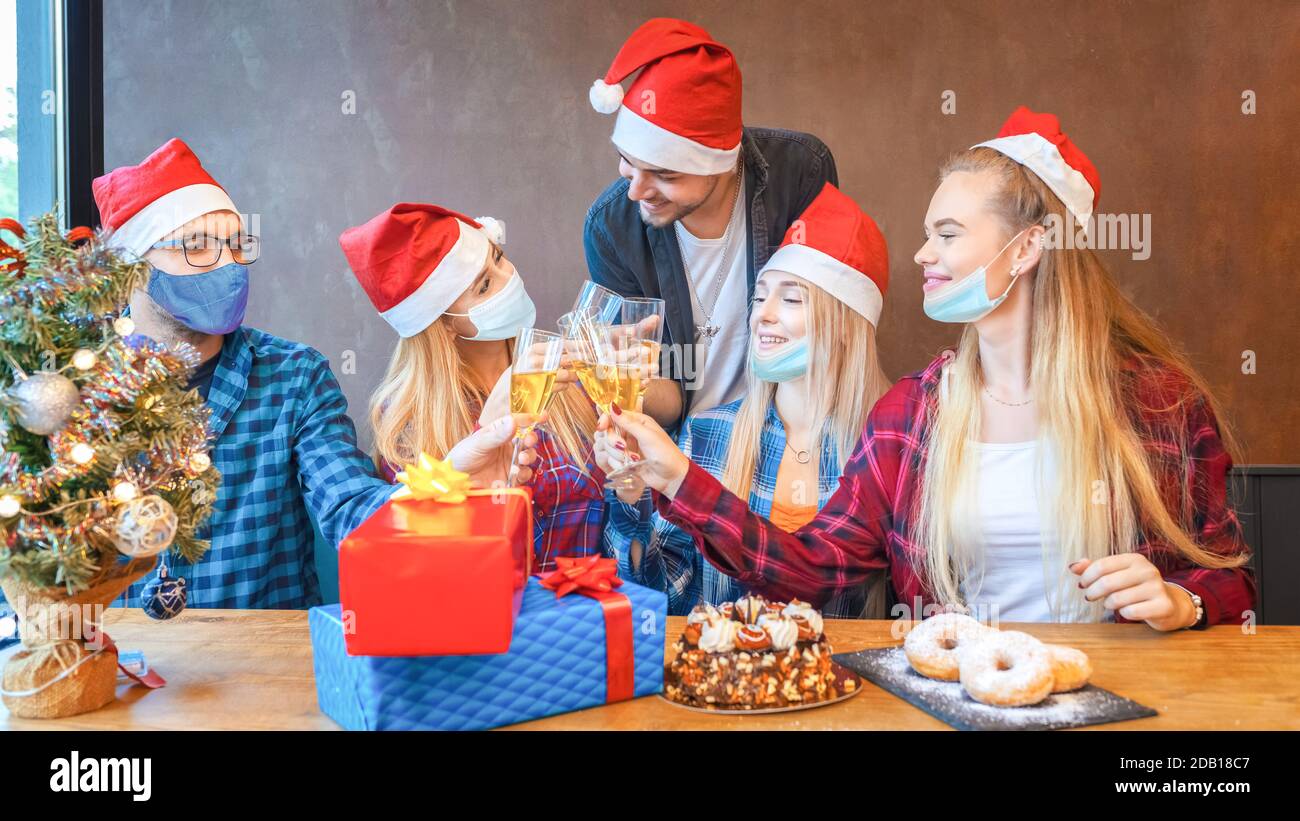 Eine Gruppe von glücklichen jungen Freunden mit Gesichtsmasken feiern Weihnachten Zusammen Champagner trinken zu Hause Isolation Stockfoto