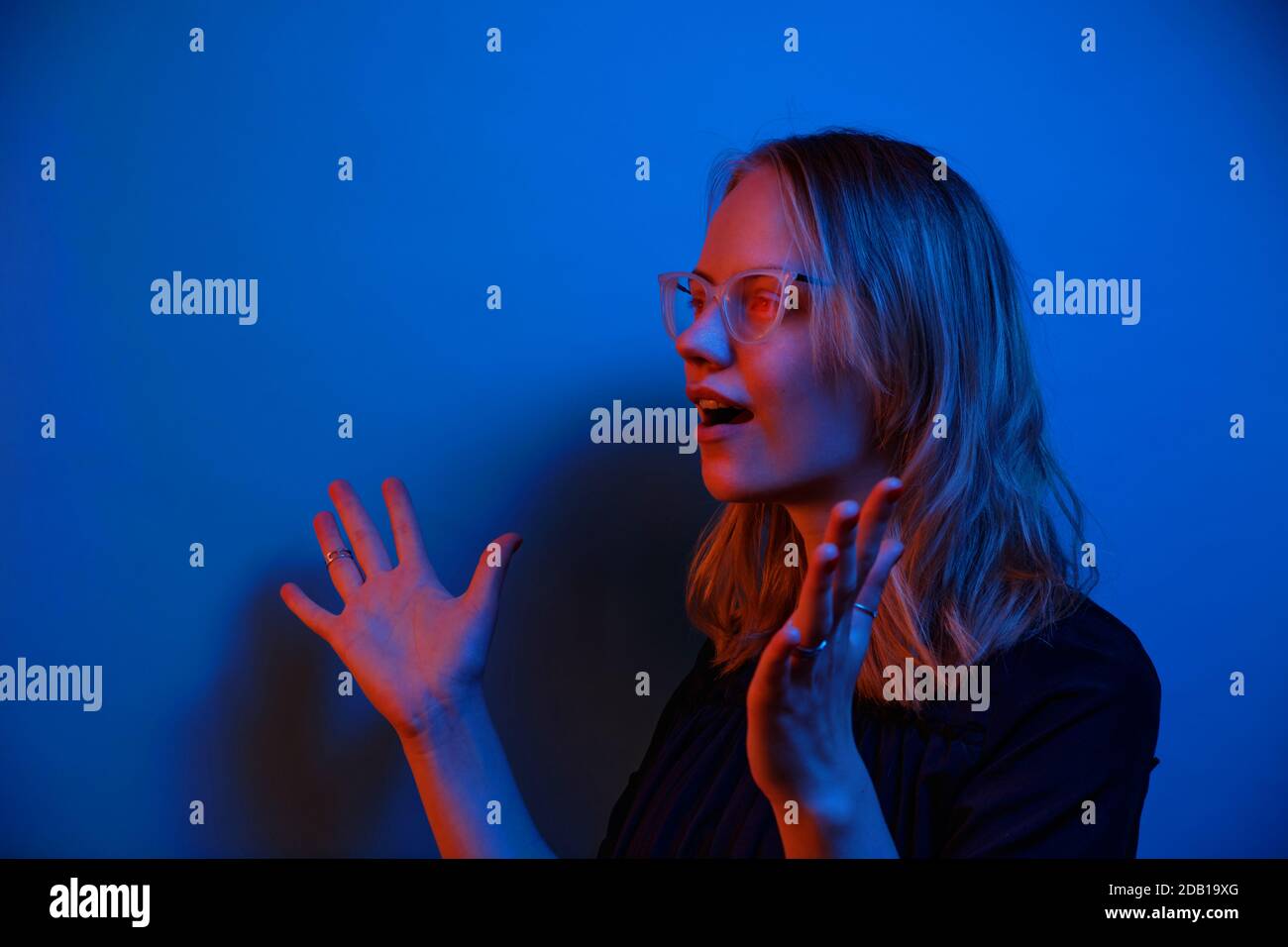 Ein junges kaukasisches Mädchen in Brille sieht auf einem dunkelblauen Neon-Hintergrund überraschend zur Seite. Menschliche Emotion Konzept und Raum kopieren. Stockfoto