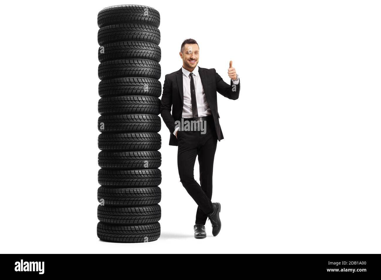 Ganzkörperportrait eines Mannes in einem schwarzen Anzug Sich auf einen Haufen Reifen lehnend und Daumen nach oben zeigend Isoliert auf weißem Hintergrund Stockfoto