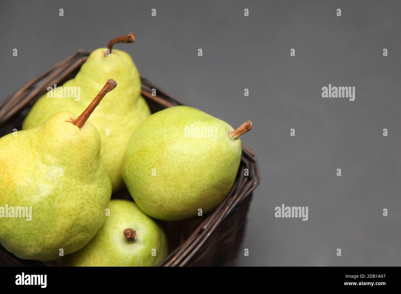 Grüne Birnen in einem Weidenkorb auf dunklem Hintergrund Stockfoto