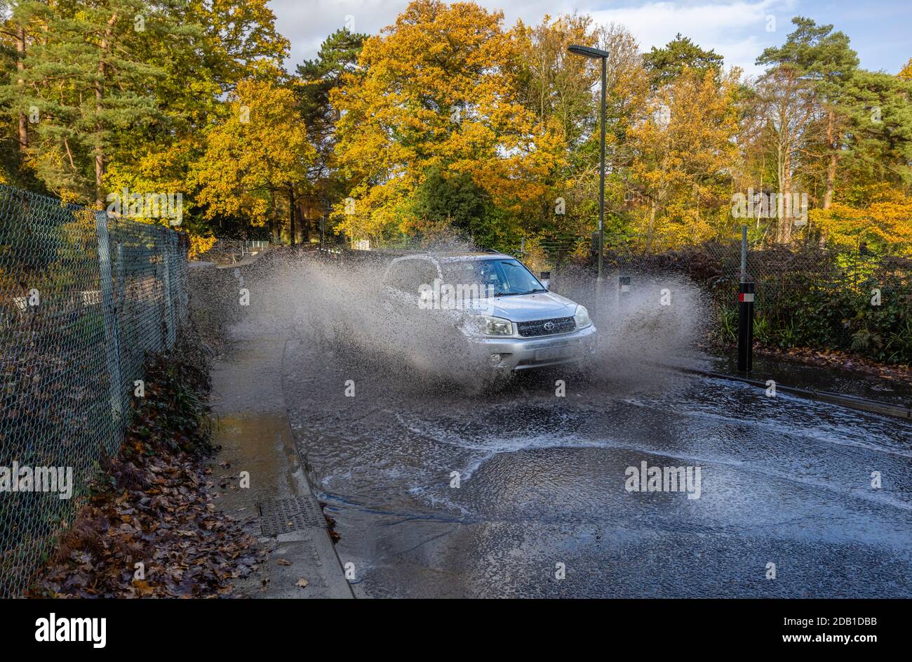Ein Auto spritzt eine Wolke Wasser und Spray Von Hochwasser in der Straße aufgrund von Überschwemmungen auf Eine Brücke über einen Eisenbahnschnitt in Woking in Bad Wetter Stockfoto
