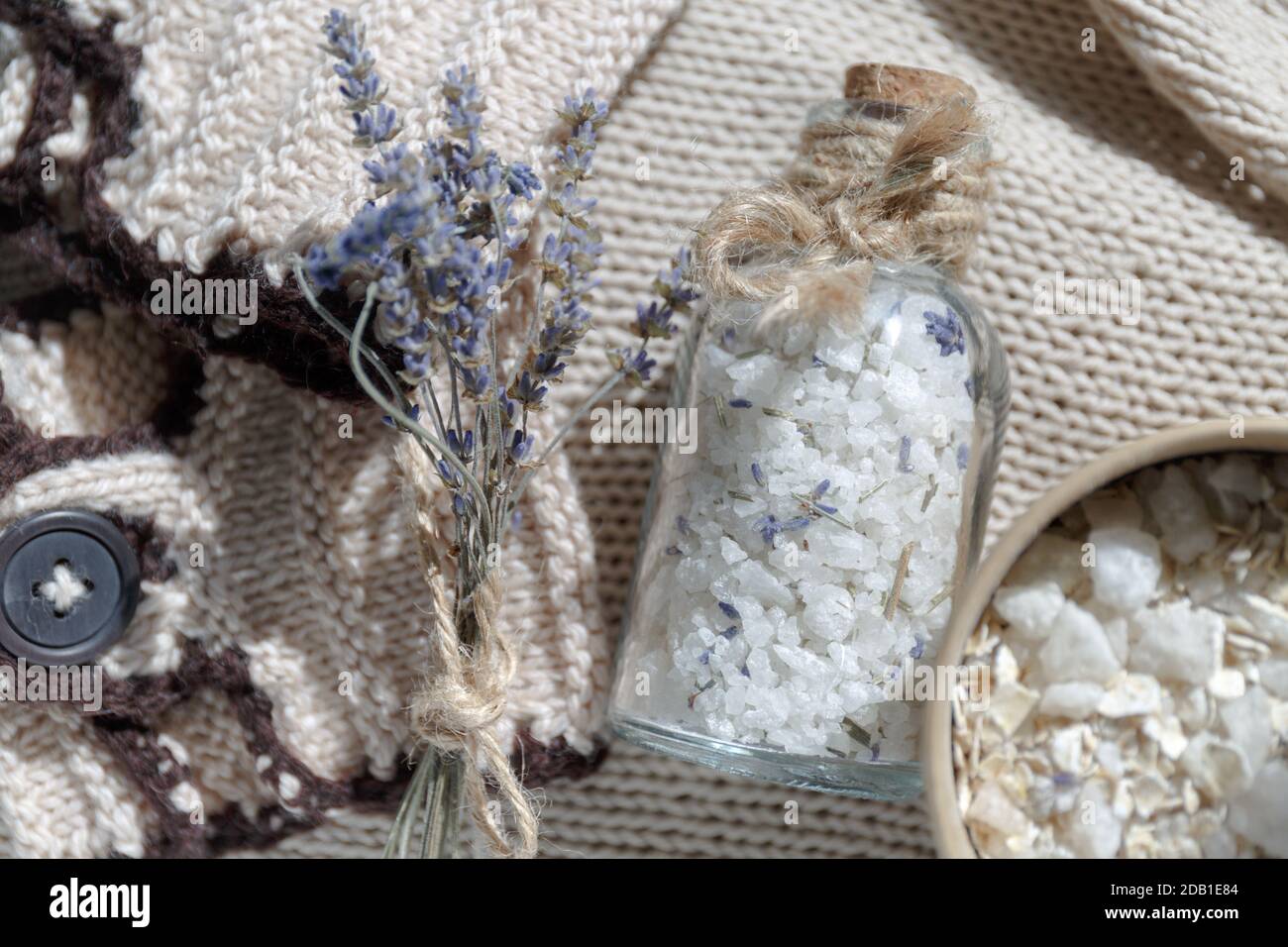 Eine Glasflasche Meersalz für ein entspannendes Bad Auf einem beigefarbenen Textil-Strickhintergrund neben einem kleinen Duft von Lavendel Stockfoto