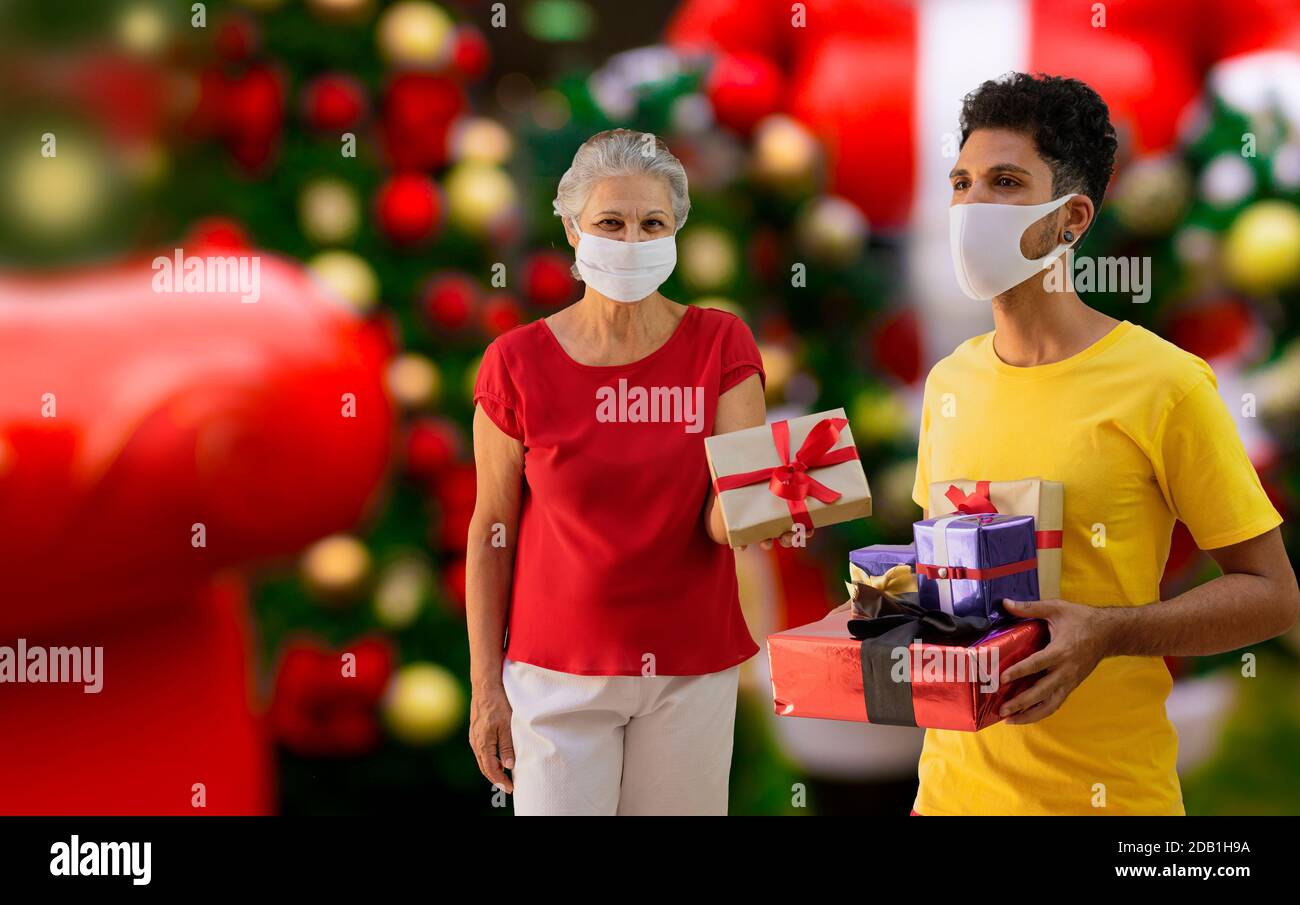 Mann und Frau mit Pandemiemaske, die ein Geschenk hält Ein heiraten weihnachten Hintergrund Konzept Bild Stockfoto