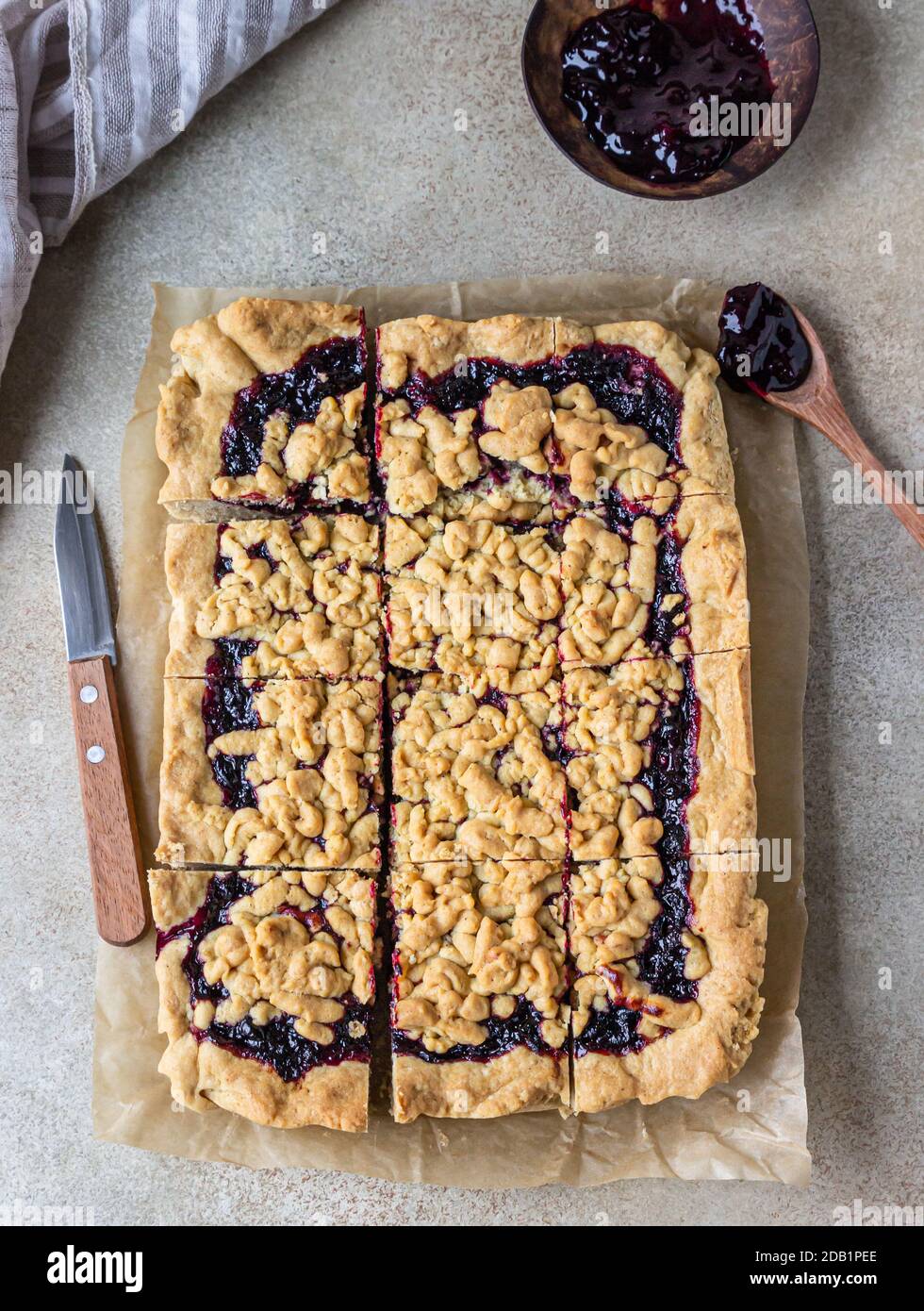 Hausgemachter Mürbeton Beeren Marmelade Kuchen auf Backpapier, heller Beton Hintergrund. Zerbröseln Sie den Kuchen. Stockfoto