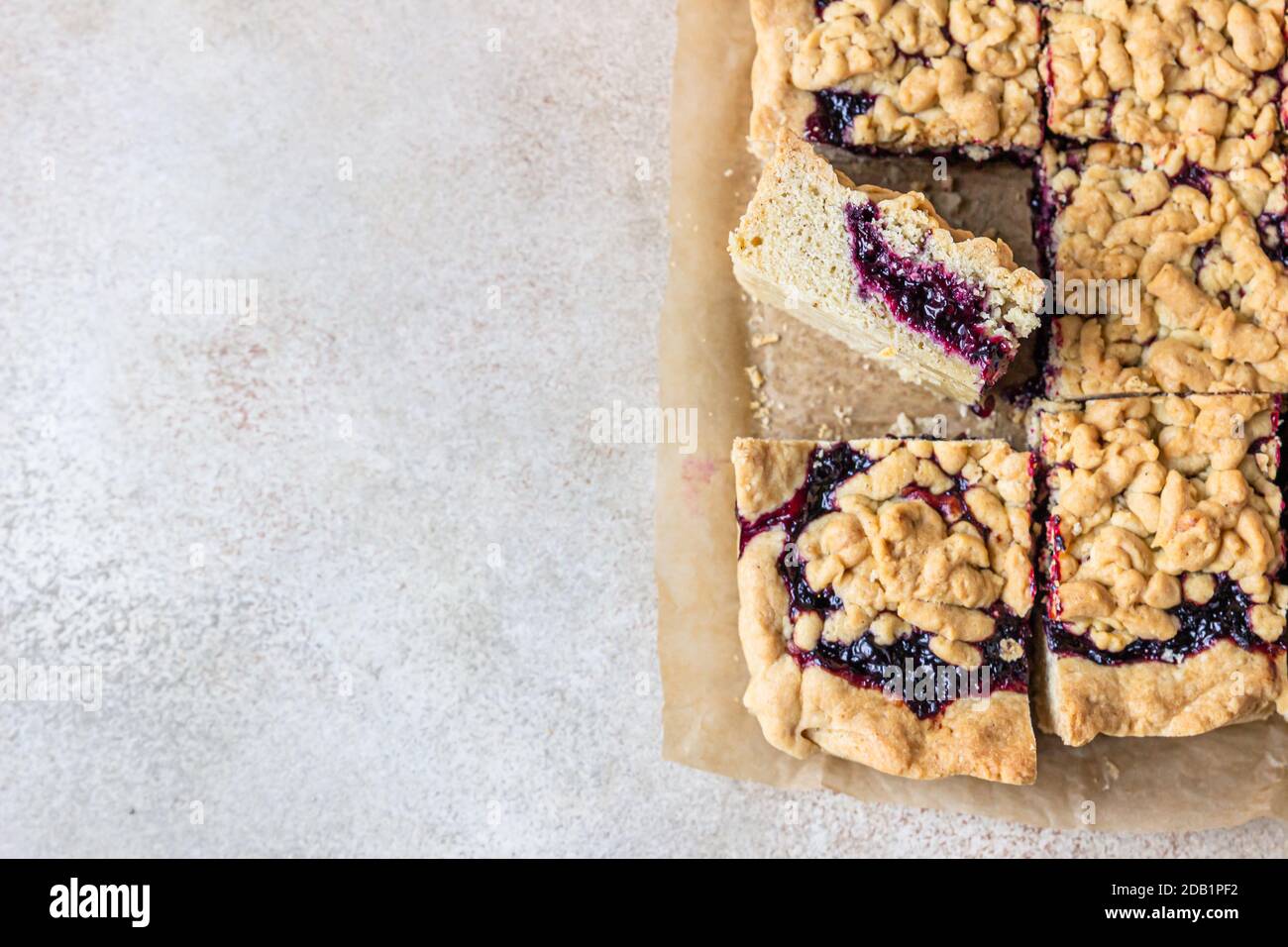 Hausgemachter Mürbeton Beeren Marmelade Kuchen auf Backpapier, heller Beton Hintergrund. Zerbröseln Sie den Kuchen. Stockfoto