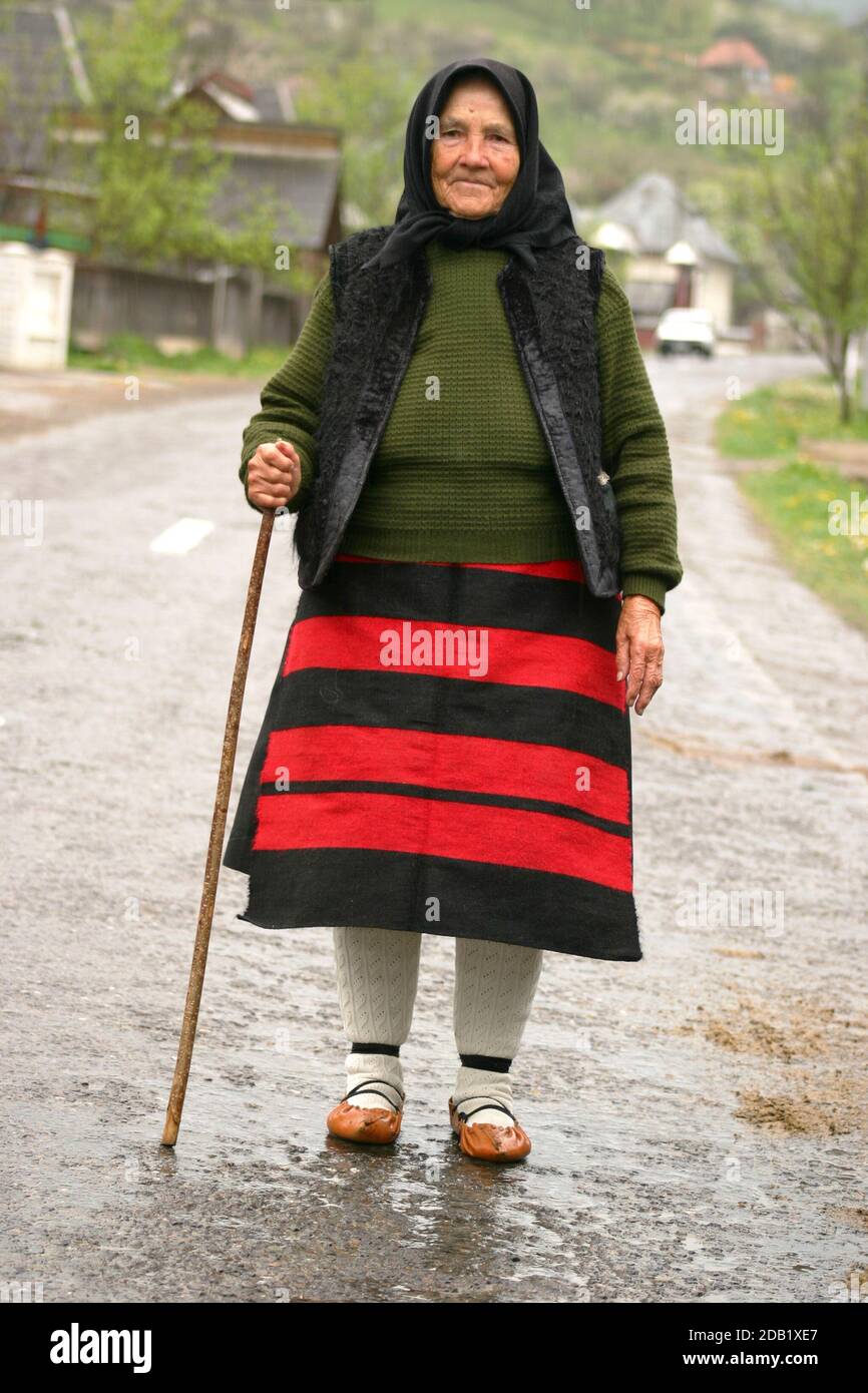 Maramures, Rumänien. Ältere Frau in traditioneller Kleidung, die mit einem Stock auf der Dorfstraße läuft. Stockfoto