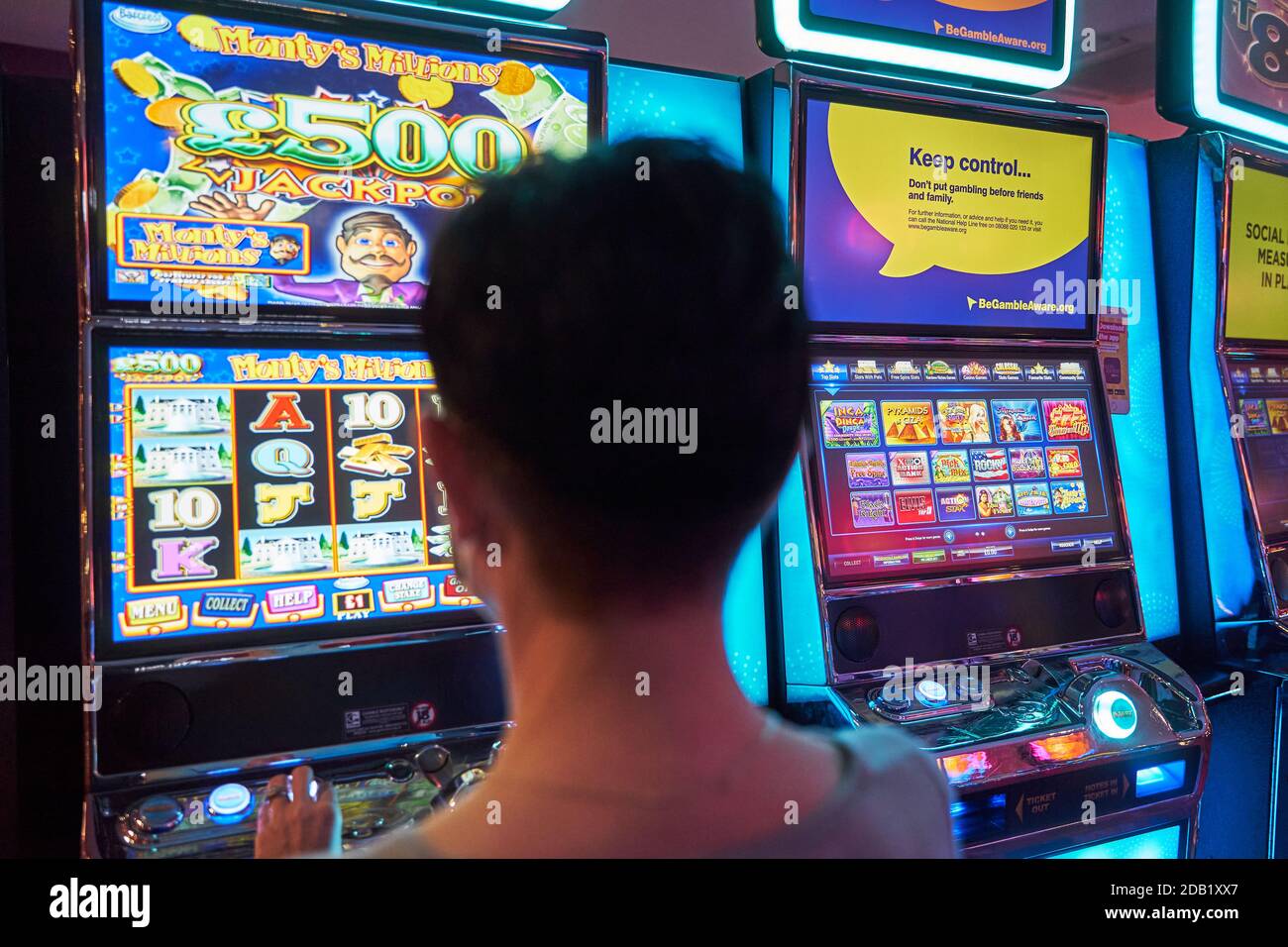 Spielautomaten spielen. Buntes Bild des Hinterkopfes des weiblichen Glücksspiels, der einen bewaffneten Banditen in einer Spielhalle betrachtet. Stockfoto