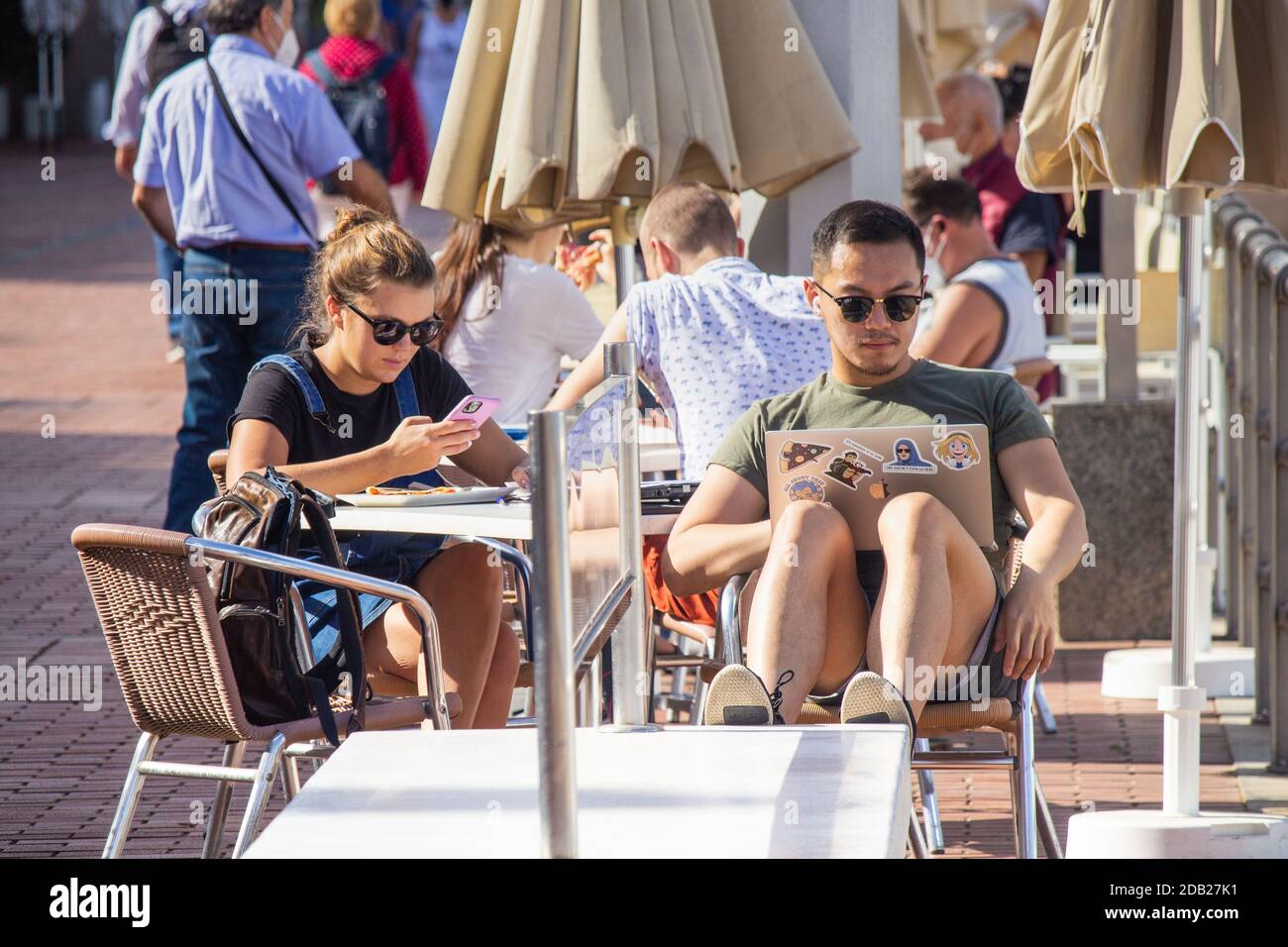 Las Palmas, Gran Canaria, Kanarische Inseln, Spanien. November 2020. Strandbüro: Ein Tourist mit Laptop im Café mit Blick auf den Stadtstrand in Las Palmas auf Gran Canaria, wenn das Thermometer 34 Grad Celcius erreicht. Ab dem 23. November müssen Personen, die von Hochrisiko-Destinationen (einschließlich Großbritannien) auf die Kanarischen Inseln kommen, innerhalb von 72 Stunden vor ihrer Ankunft in Spanien ein negatives Covid-Ergebnis vorbringen. Kredit: Alan Dawson/Alamy Live Nachrichten Stockfoto