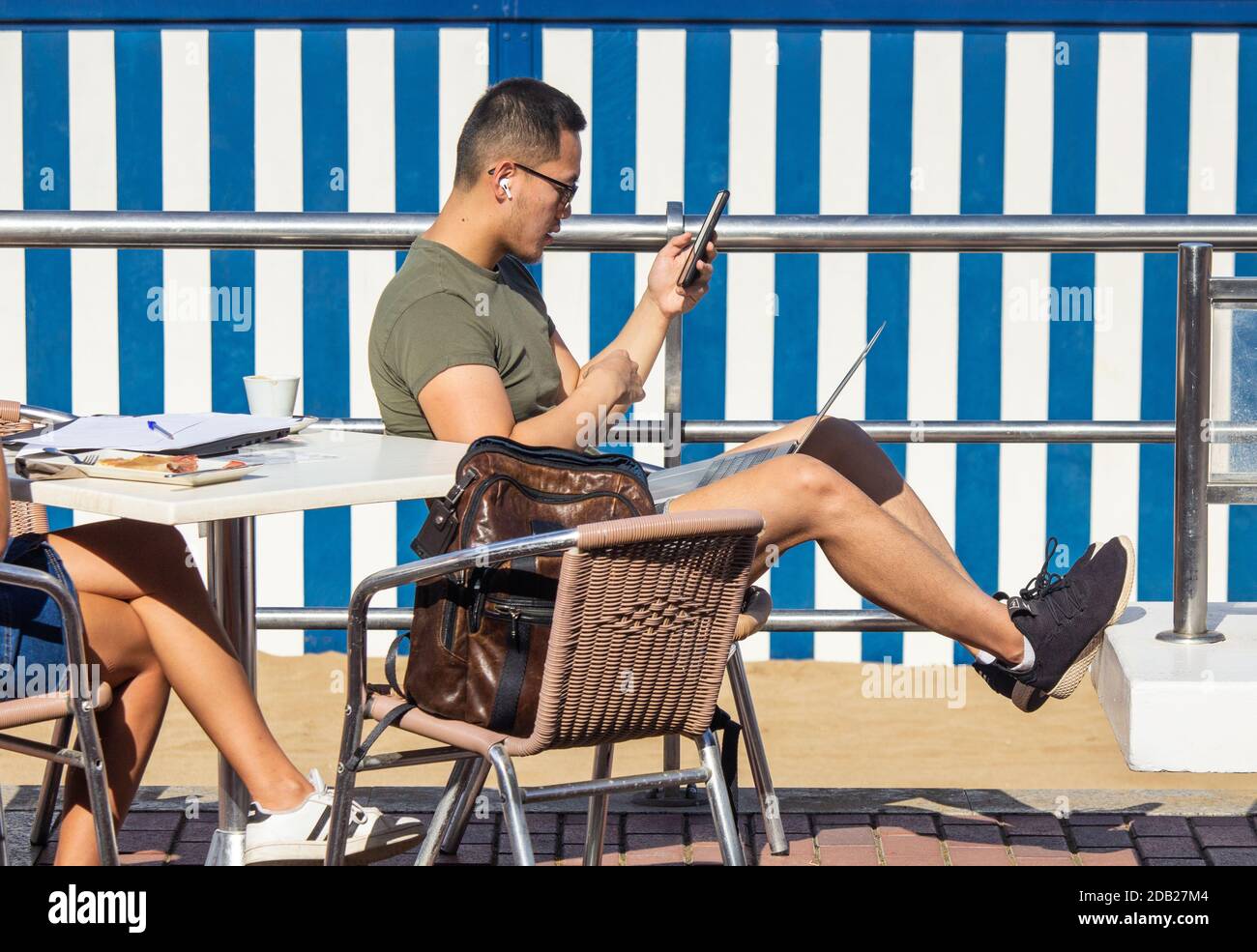 Las Palmas, Gran Canaria, Kanarische Inseln, Spanien. November 2020. Strandbüro: Ein Tourist mit Laptop im Café mit Blick auf den Stadtstrand in Las Palmas auf Gran Canaria, wenn das Thermometer 34 Grad Celcius erreicht. Ab dem 23. November müssen Personen, die von Hochrisiko-Destinationen (einschließlich Großbritannien) auf die Kanarischen Inseln kommen, innerhalb von 72 Stunden vor ihrer Ankunft in Spanien ein negatives Covid-Ergebnis vorbringen. Kredit: Alan Dawson/Alamy Live Nachrichten Stockfoto