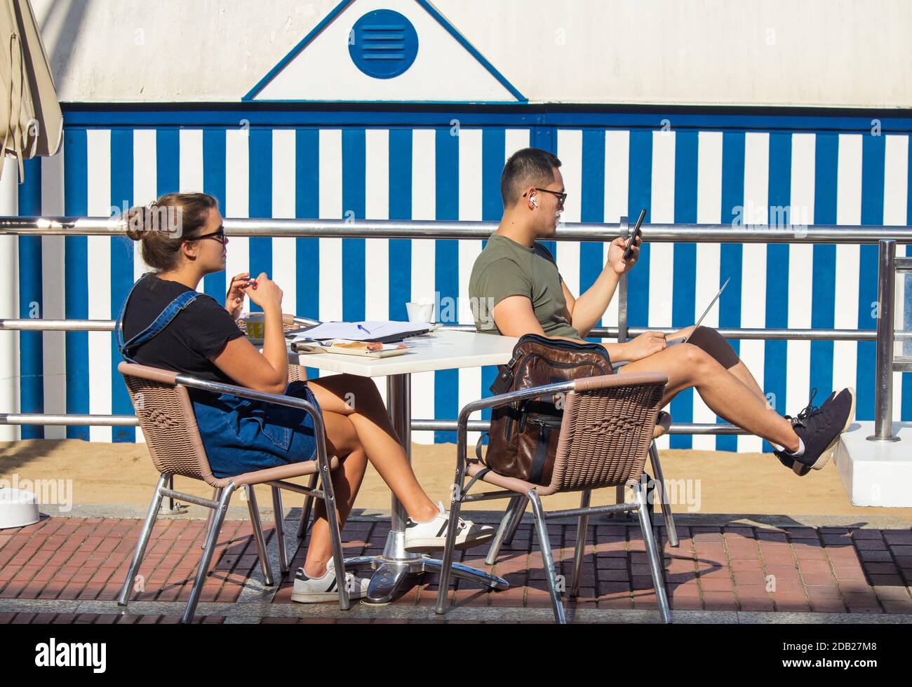 Las Palmas, Gran Canaria, Kanarische Inseln, Spanien. November 2020. Strandbüro: Ein Tourist mit Laptop im Café mit Blick auf den Stadtstrand in Las Palmas auf Gran Canaria, wenn das Thermometer 34 Grad Celcius erreicht. Ab dem 23. November müssen Personen, die von Hochrisiko-Destinationen (einschließlich Großbritannien) auf die Kanarischen Inseln kommen, innerhalb von 72 Stunden vor ihrer Ankunft in Spanien ein negatives Covid-Ergebnis vorbringen. Kredit: Alan Dawson/Alamy Live Nachrichten Stockfoto