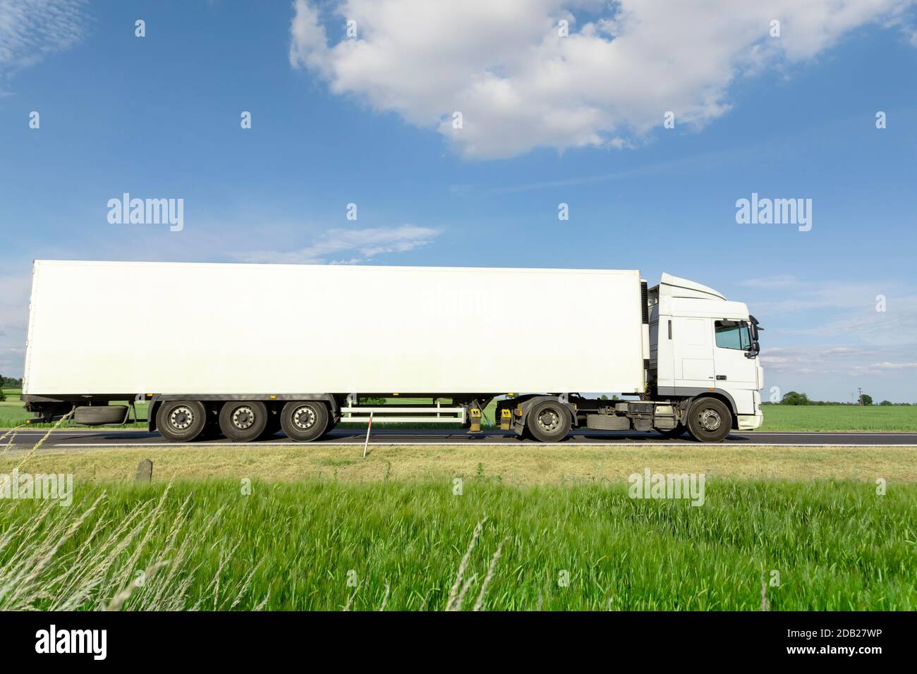 Weißer Transport-LKW fährt auf der Straße, grüne Wiese mit blauem Himmel Stockfoto