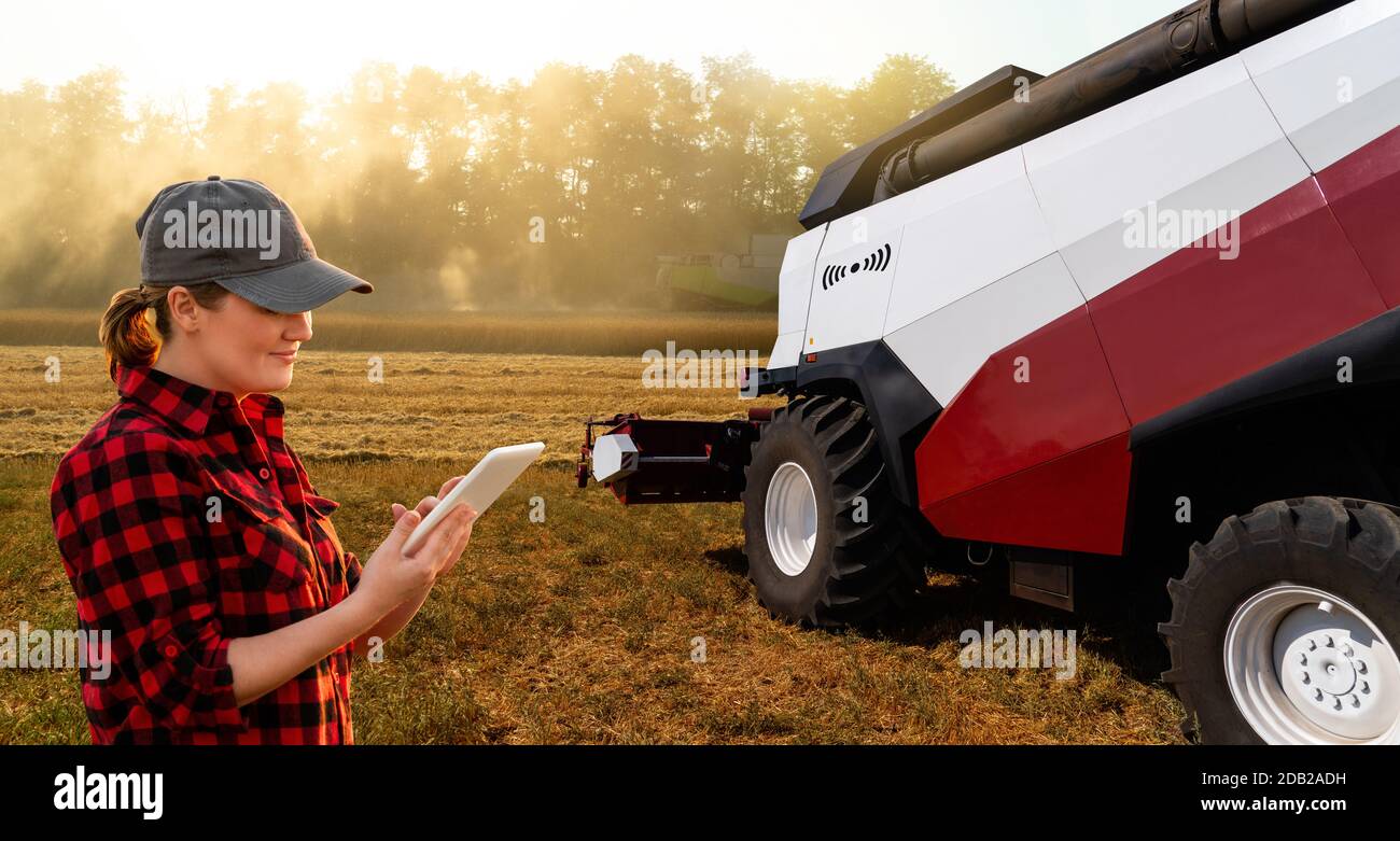 Farmer verwendet ein digitales Tablet, um den autonomen Erntemaschinen zu steuern. Smart Farming-Konzept Stockfoto