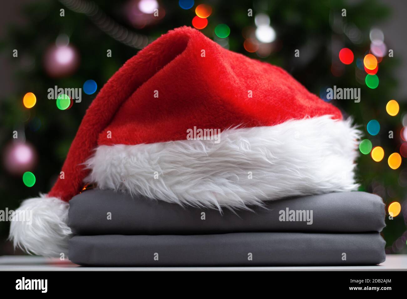 Ein Stapel gefalteter Bettlaken mit einem Weihnachtsmann-Hut vor dem Hintergrund eines Weihnachtsbaums mit Lichtern. Stockfoto