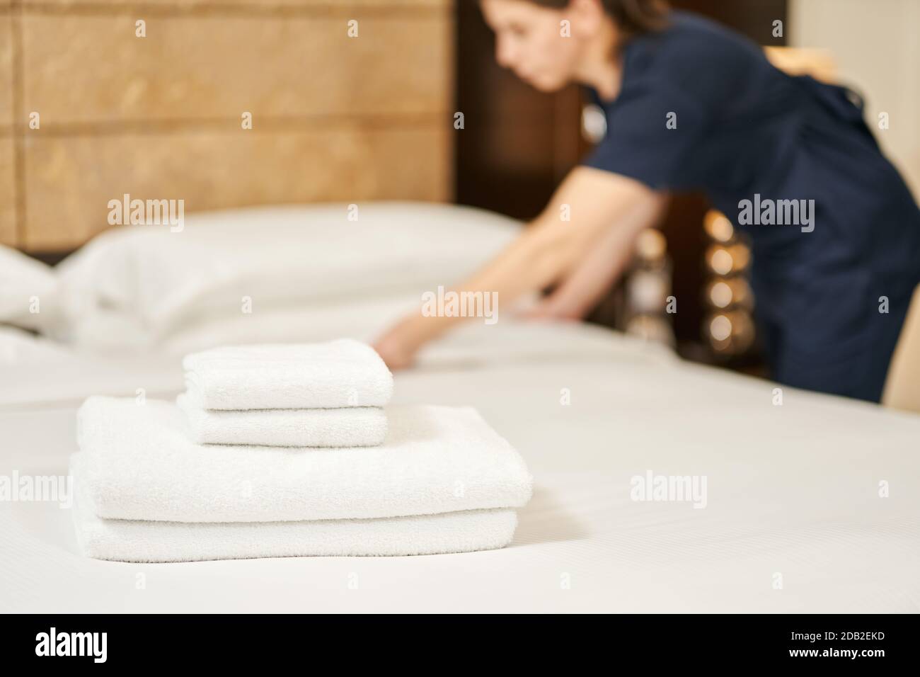 Stapel Handtücher auf dem Bett mit Zimmermädchen im Hintergrund im Hotelzimmer. Servicekonzept des Hotels Stockfoto