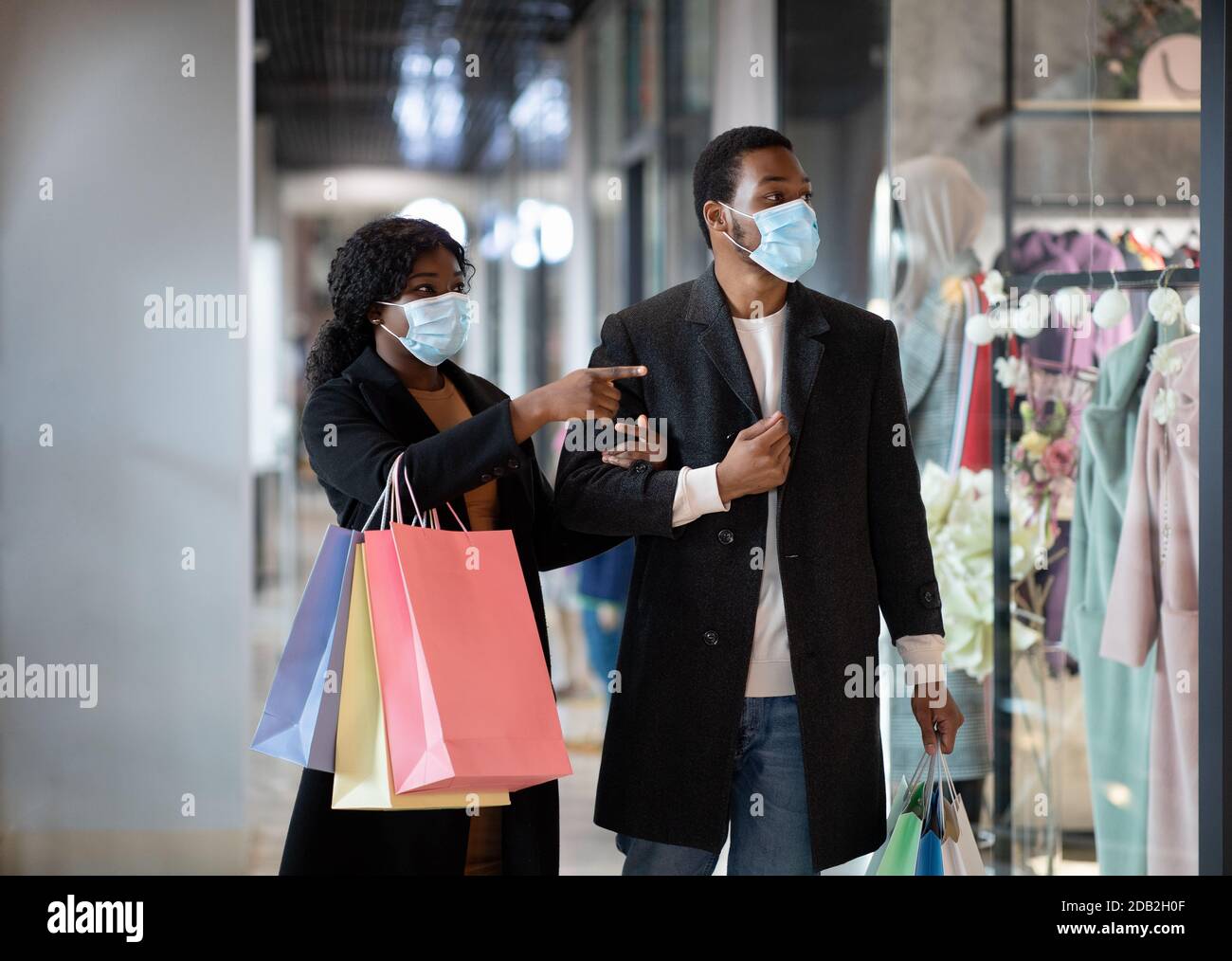 Millennial african american männlich und weiblich in Mänteln und medizinisch Masken nach dem Einkauf mit Paketen Stockfoto