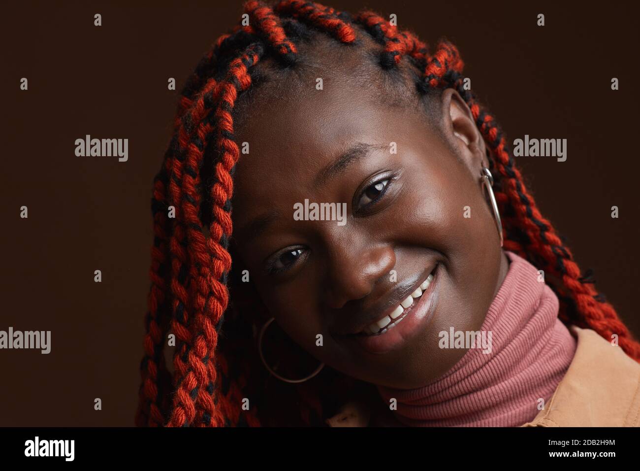 Nahaufnahme Porträt der stilvollen afroamerikanischen Frau mit geflochtenen Haaren Lächelnd, während er vor dunkelbraunem Hintergrund im Studio posiert Stockfoto