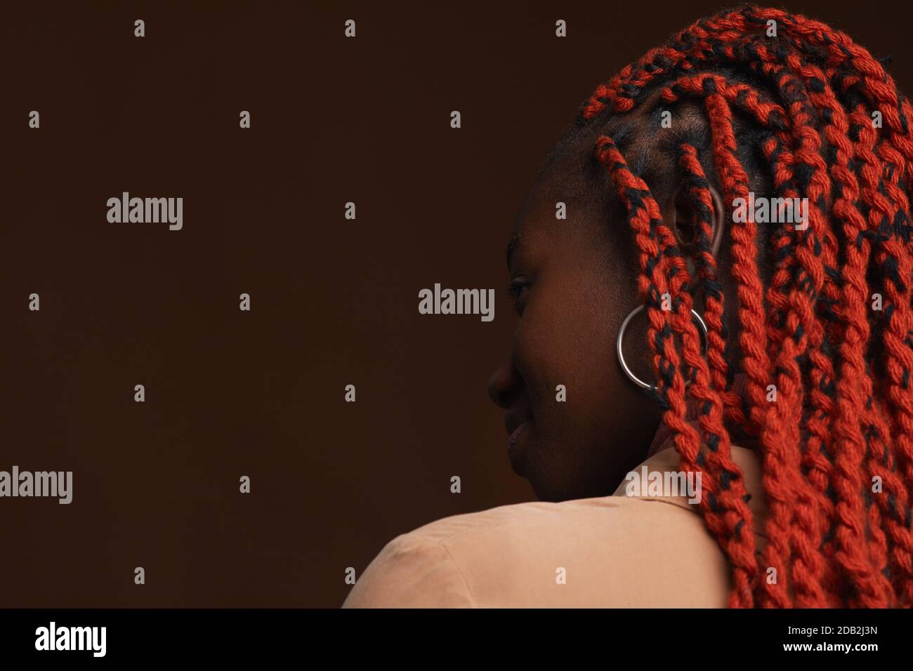 Rückansicht Porträt einer stilvollen afroamerikanischen Frau mit geflochtenen Haaren Wegschauen, während posiert vor dunkelbraunem Hintergrund im Studio Stockfoto