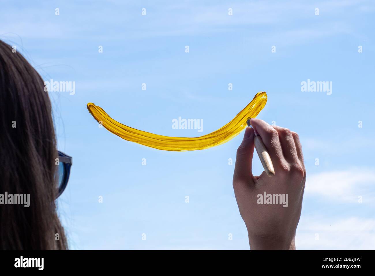 Weibliche Hand zeichnet ein lächelndes Gesicht mit Farbe auf dem Fenster gegen den blauen Himmel. Das Konzept von Glück, Gesundheit, Freude. Stockfoto